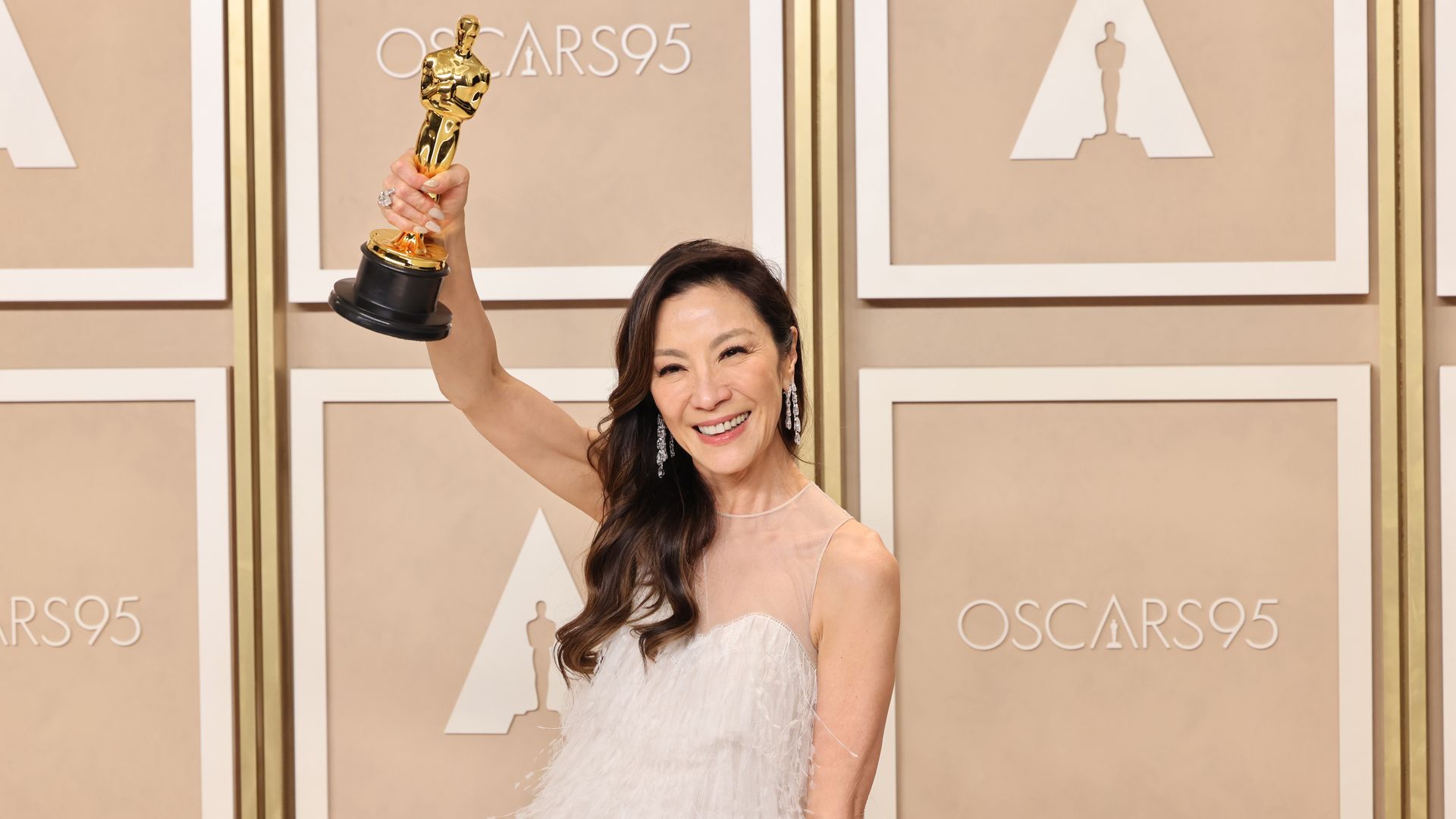 Photo of Michelle Yeoh smiling while raising her golden Oscar statue award in the press room