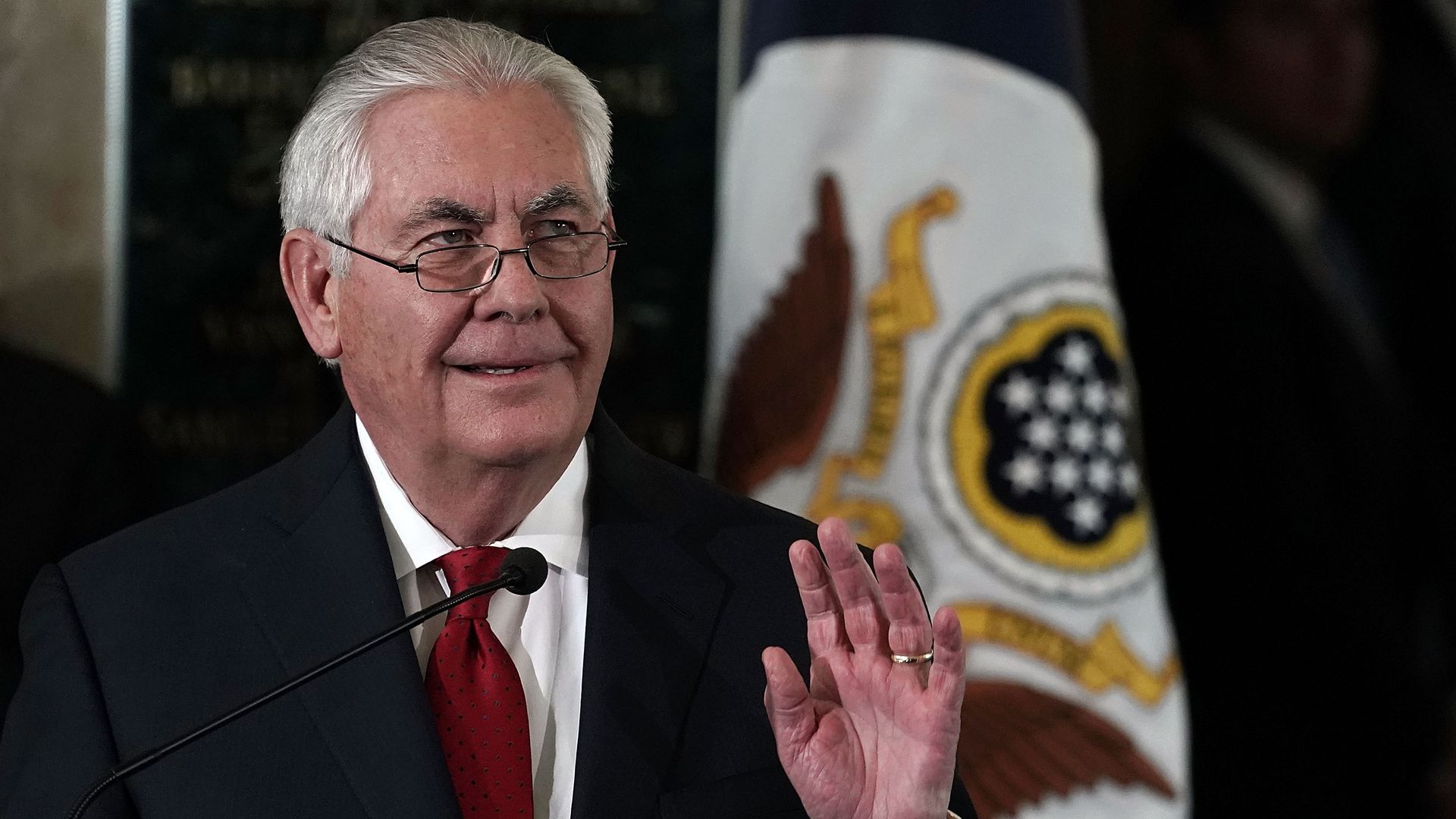 In this image, Tillerson smiles and waves while wearing a suit.