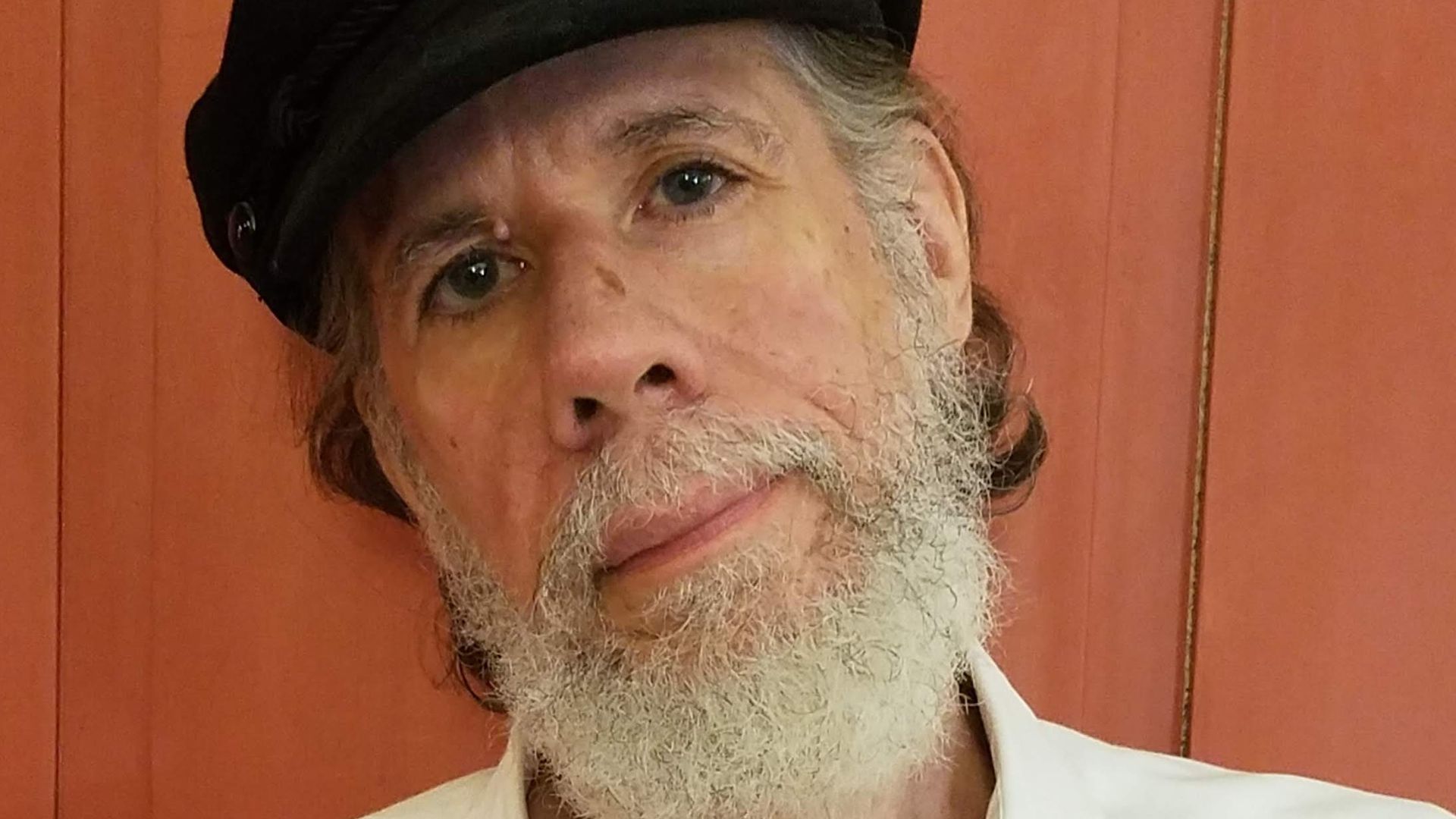 Poet Martin Espada stands for a portrait wearing  a black hat.