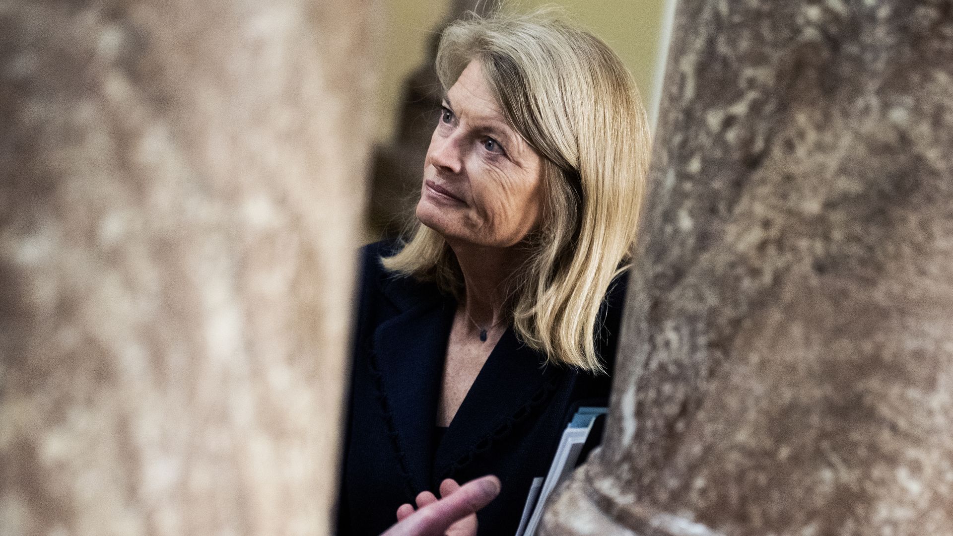 Sen. Lisa Murkowski, wearing a black dress, seen between two marble columns.
