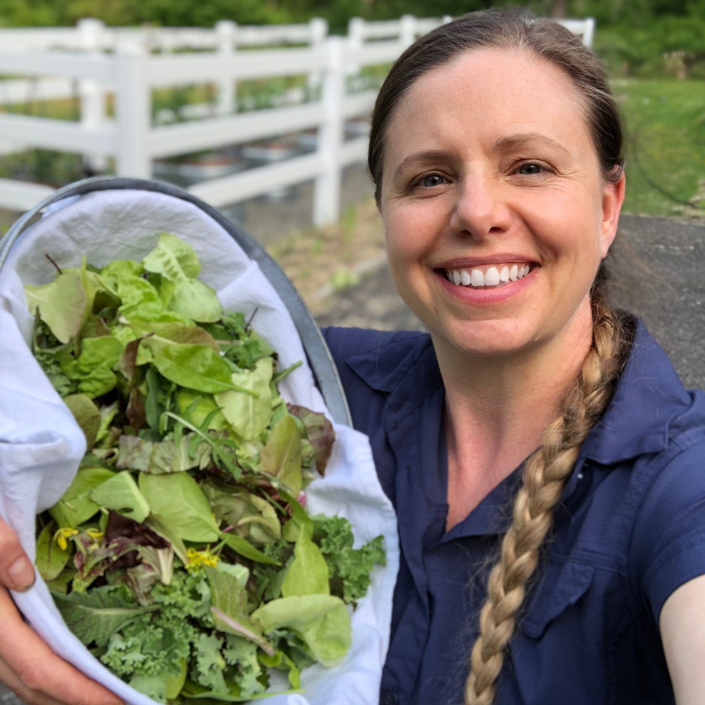 A woman with a big smile and a basket of fresh picked greens.