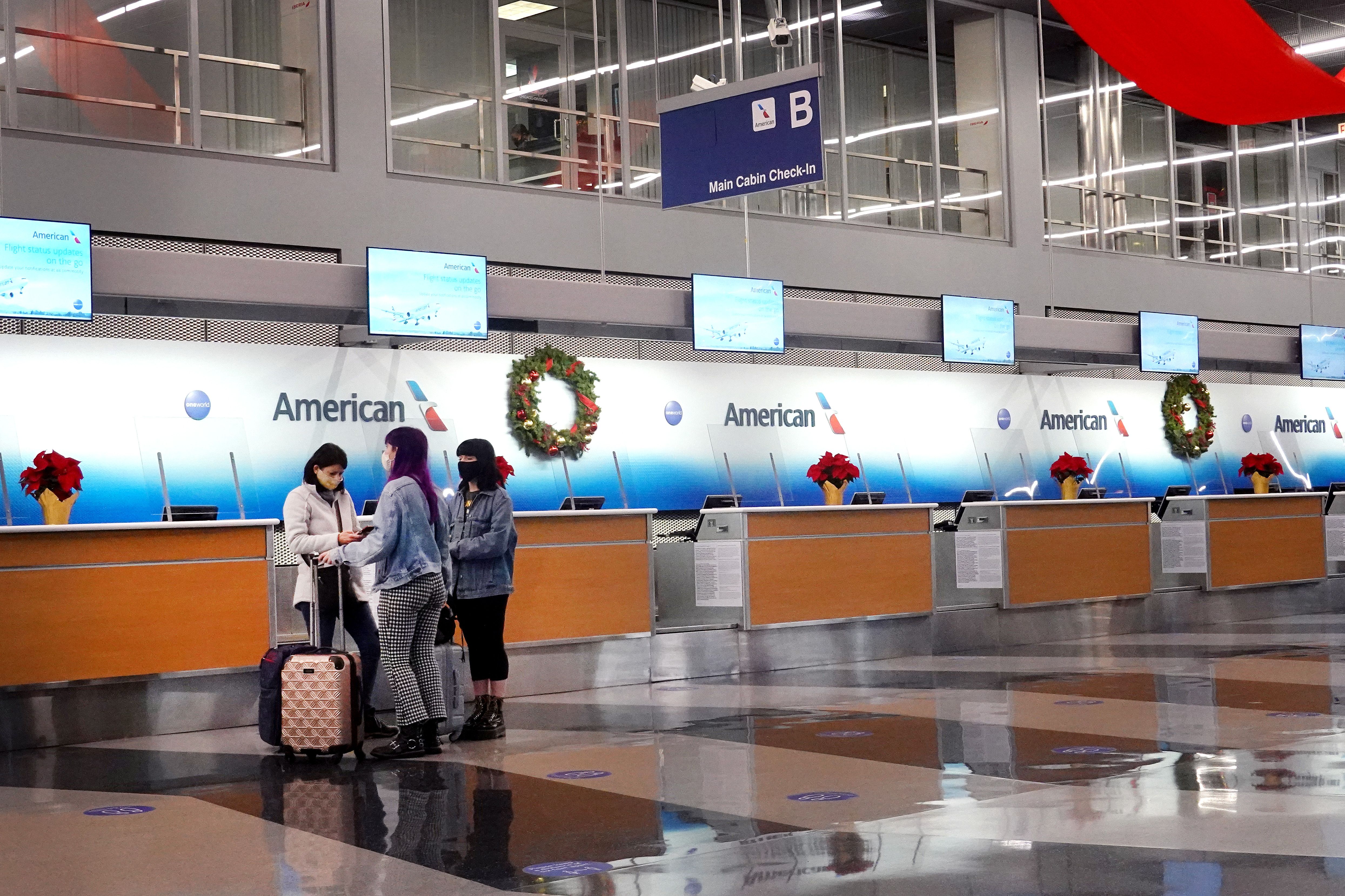 Three women stand wearing masks in front of an empty American Airlines kiosk 