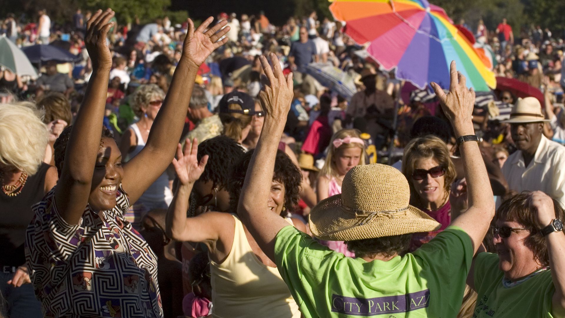 A crowd of people throw their hands in the air at a park