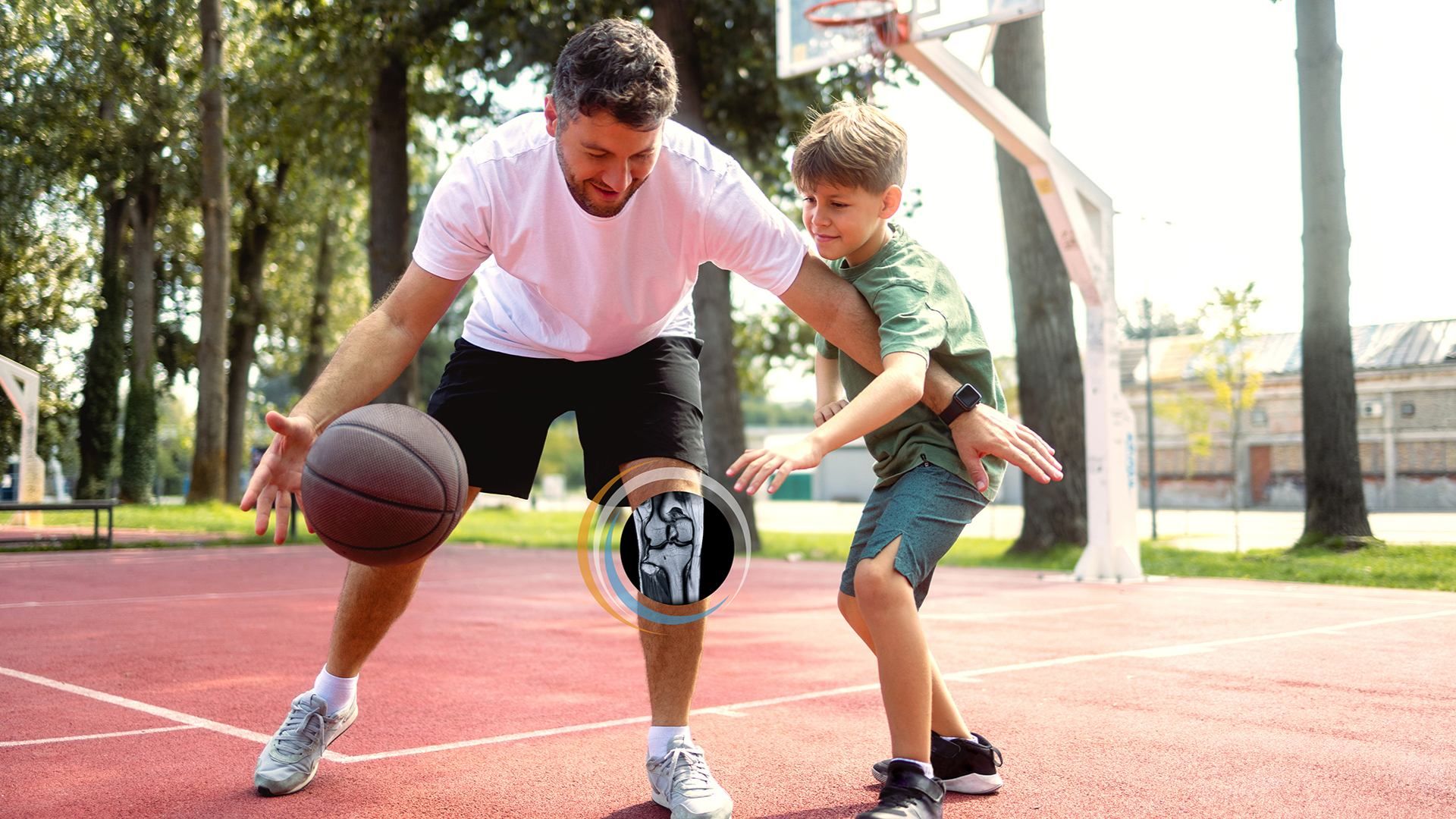 An adult man and a boy play basketball on an outdoor court. The man in a pale pink shirt dribbles the ball while the boy in green guards him, with a hoop and trees in the background.