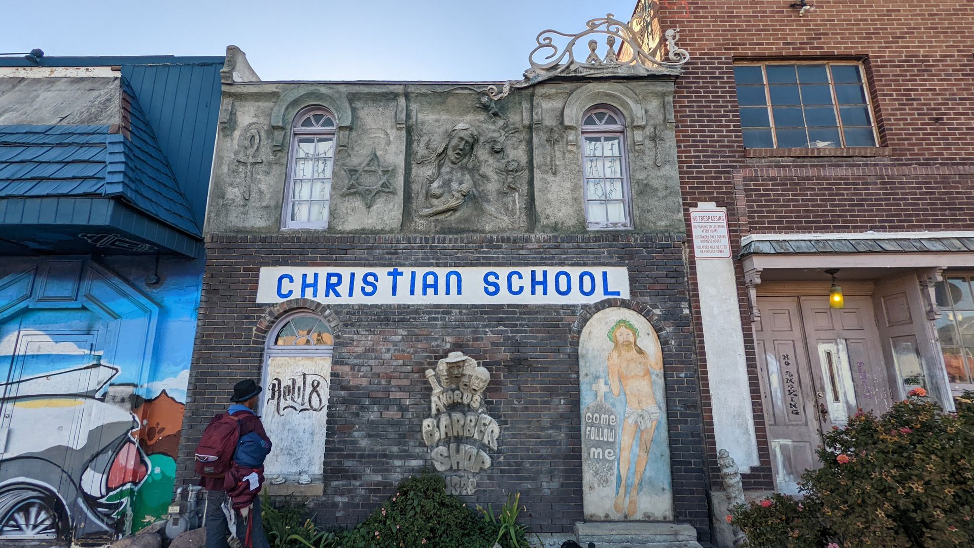 A building facade has attached sculptures of a woman, a star of David and a barbershop quartet, alongside a painting of Jesus. A sign says "Christian School." a 