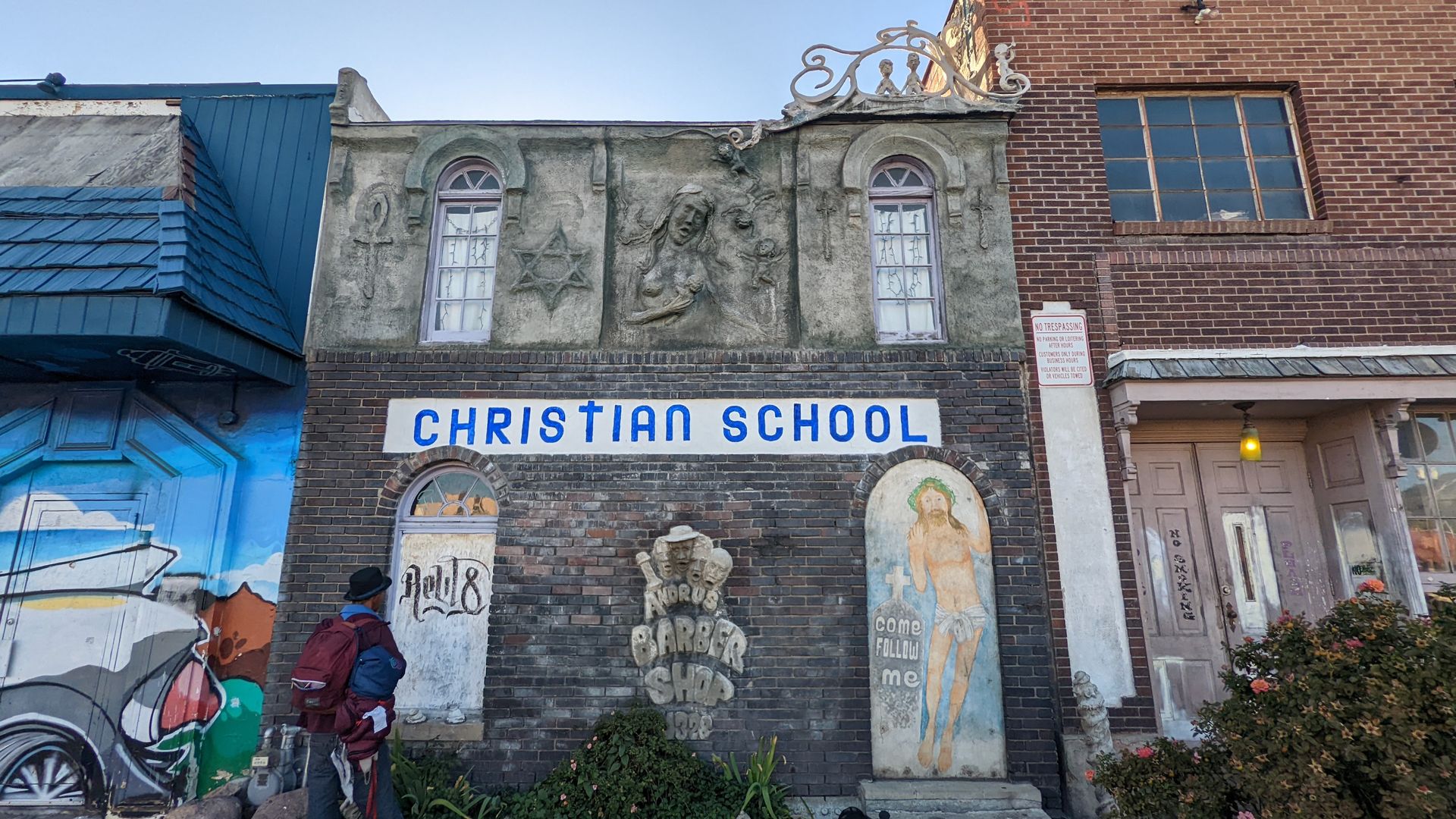 A building facade has attached sculptures of a woman, a star of David and a barbershop quartet, alongside a painting of Jesus. A sign says "Christian School." a