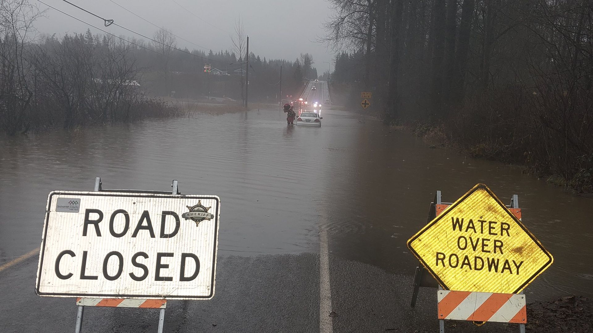 A woman stands near her partially submerged car on a road that was closed due to flooding in Snohomish County, Washington.