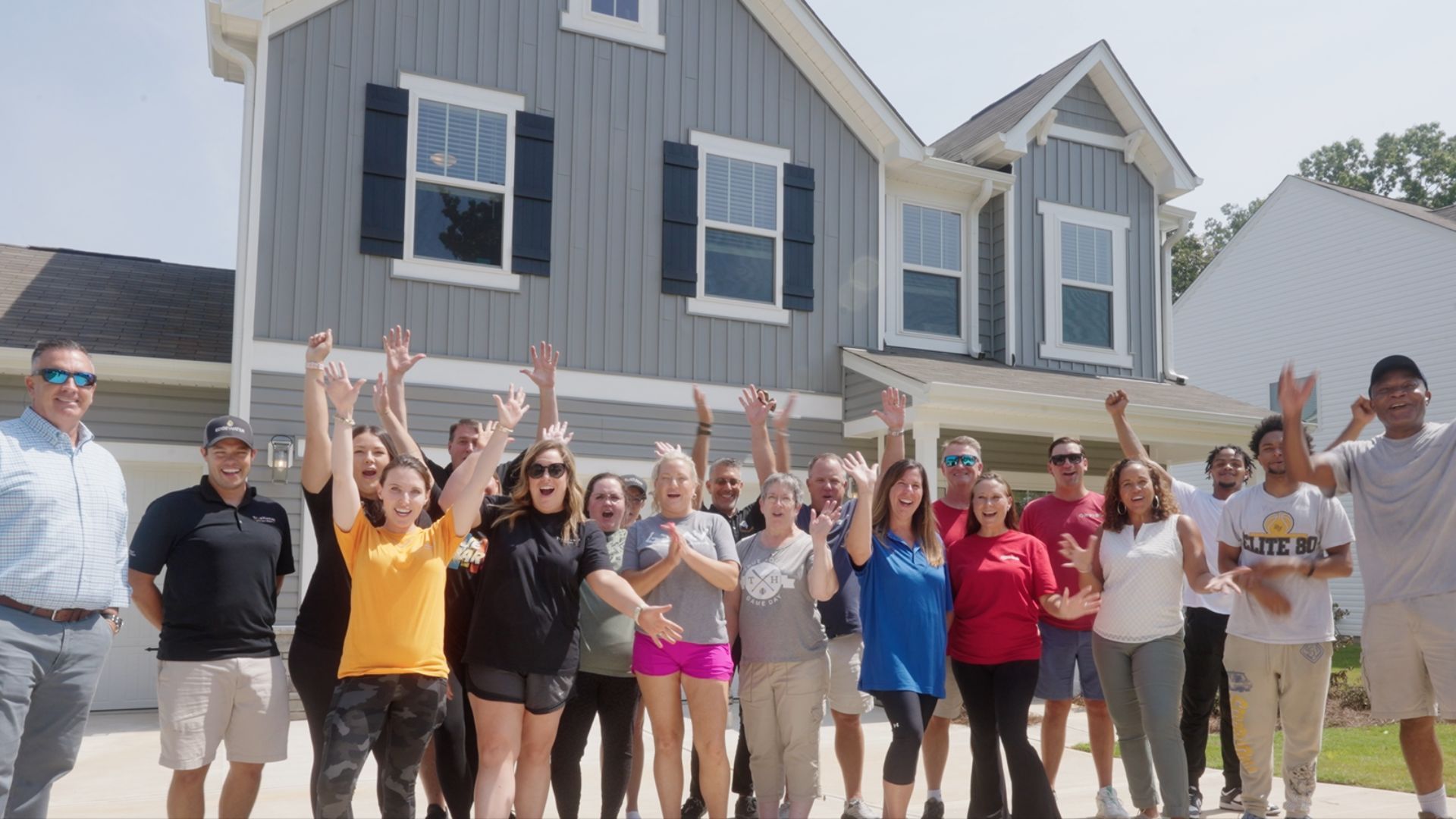 A group of people cheering in front of a house, some of them have their arms raised.