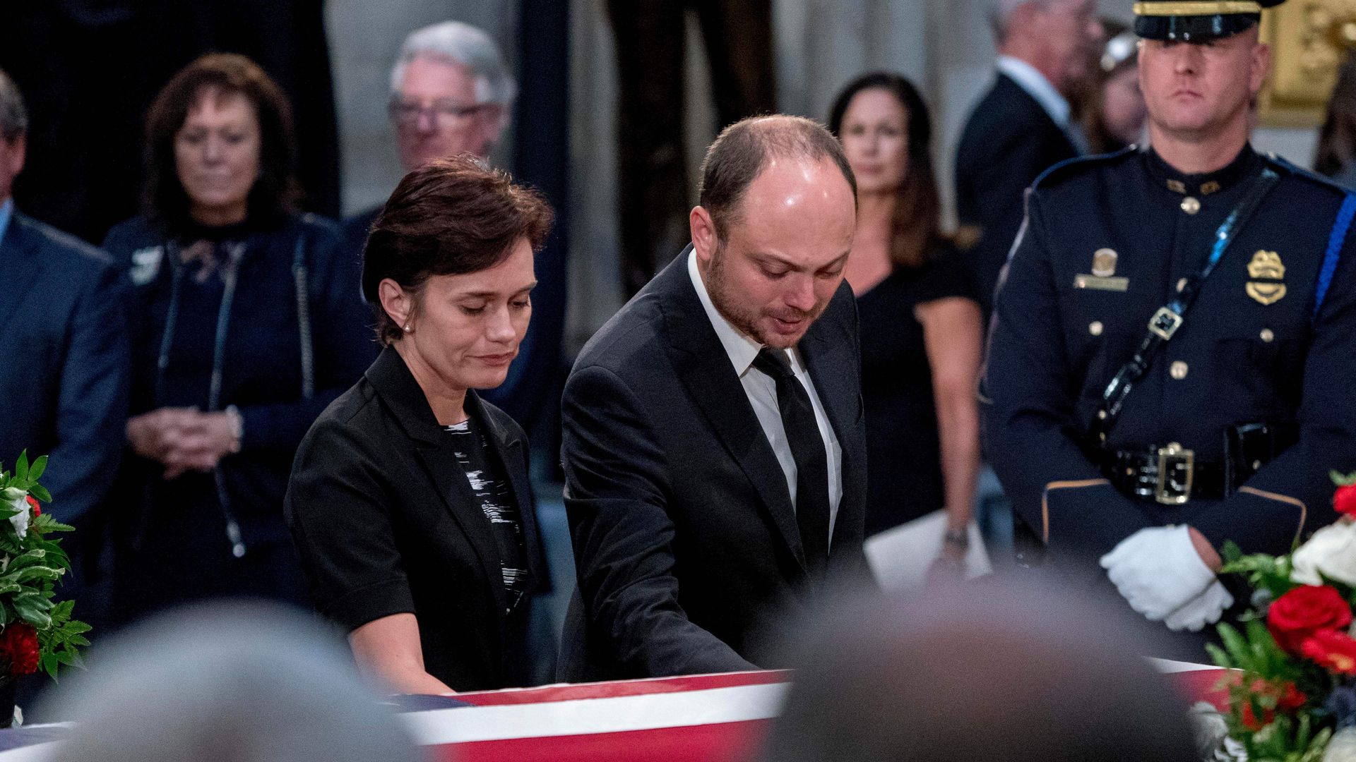 A man and a woman touch a coffin draped in an American flag.