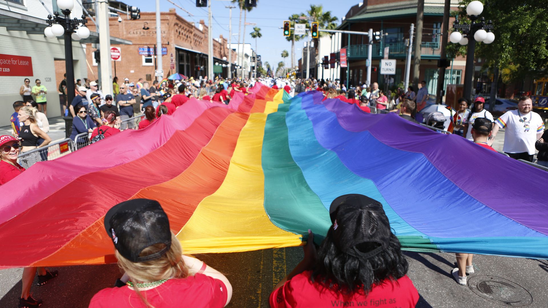 A dozen people walk along a parade route holding a giant rainbow Pride flag.