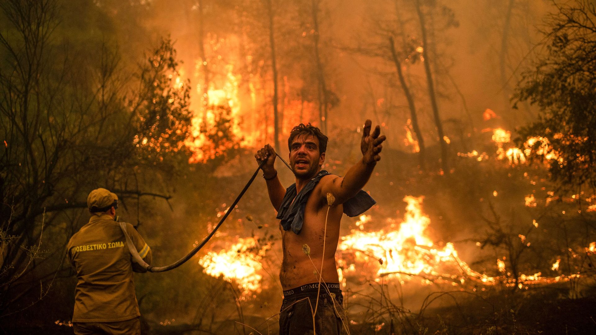 A local resident gestures as he holds an empty water hose during an attempt to extinguish forest fires