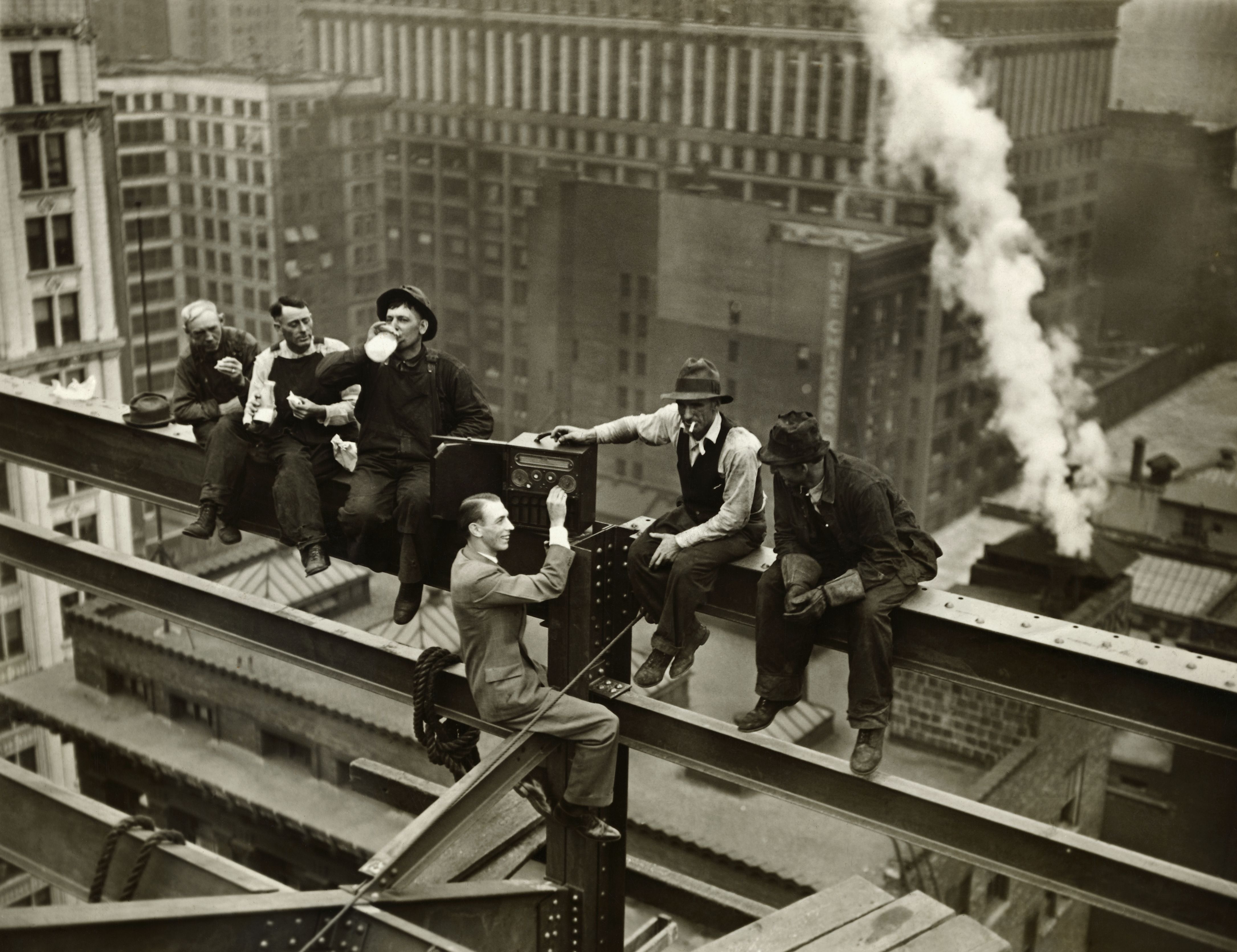 Photo of men listening to radio while on construction beams high in the sky. 
