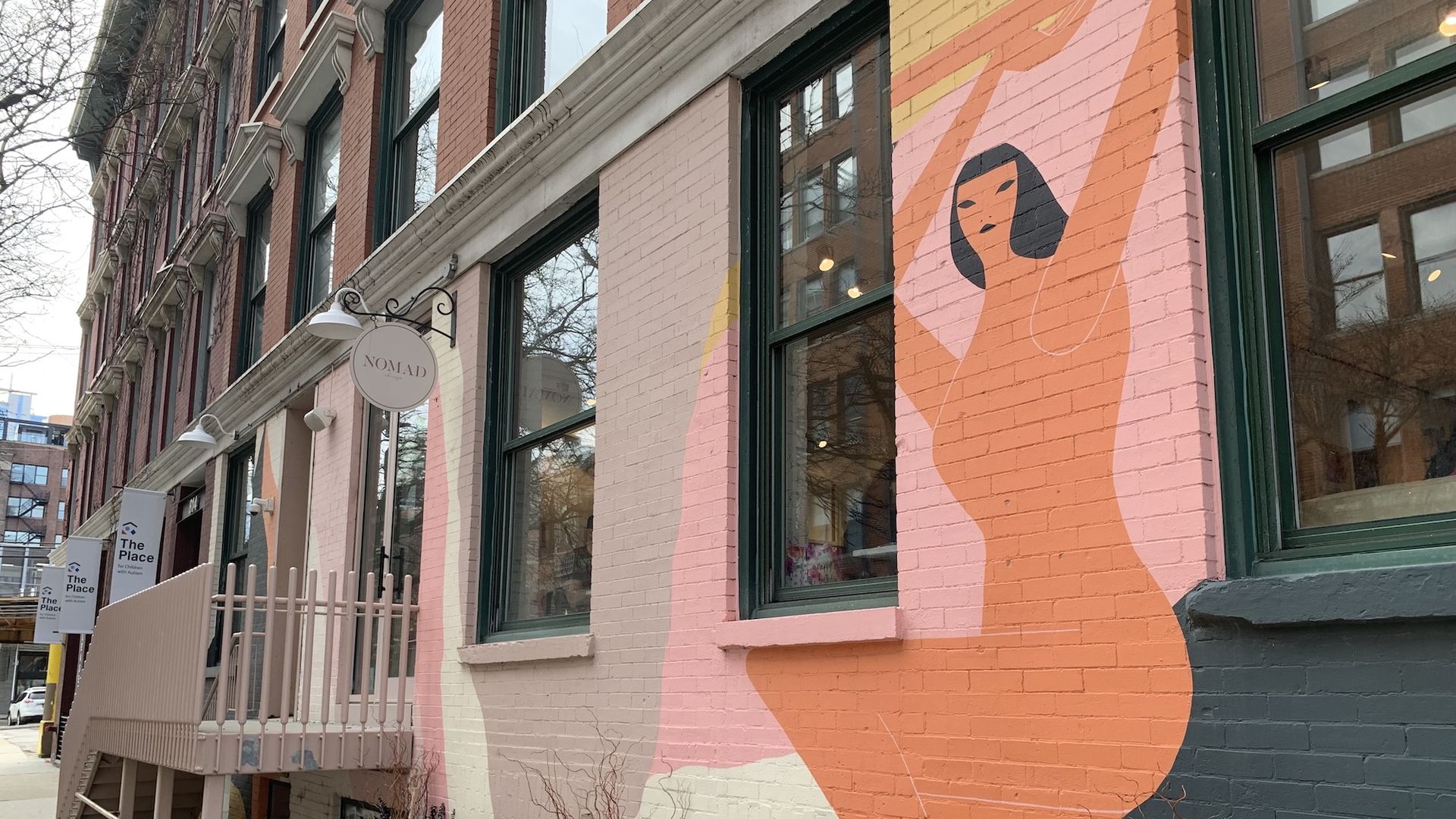 Exterior of brick building with a painting of a woman on it.