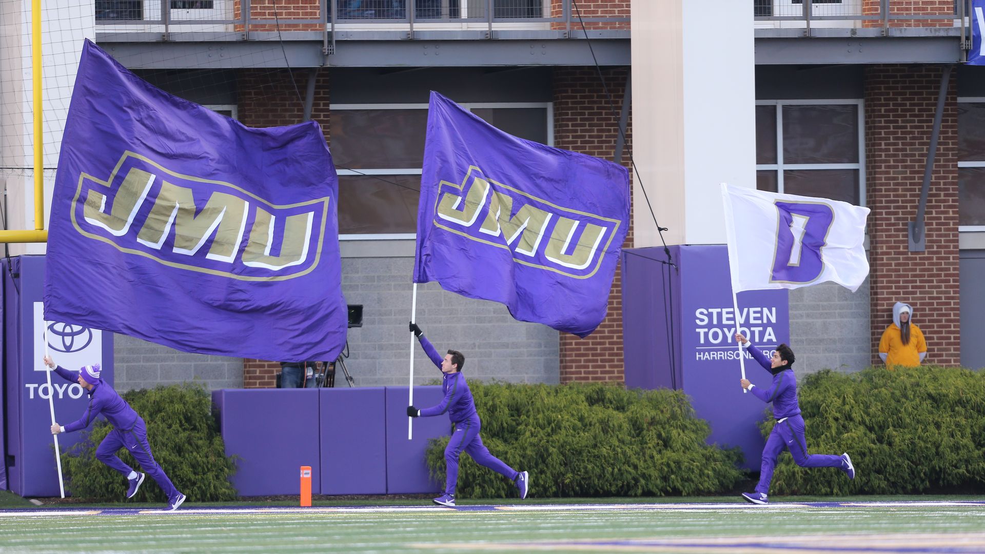 people holding JMU flags while running across the football field. 