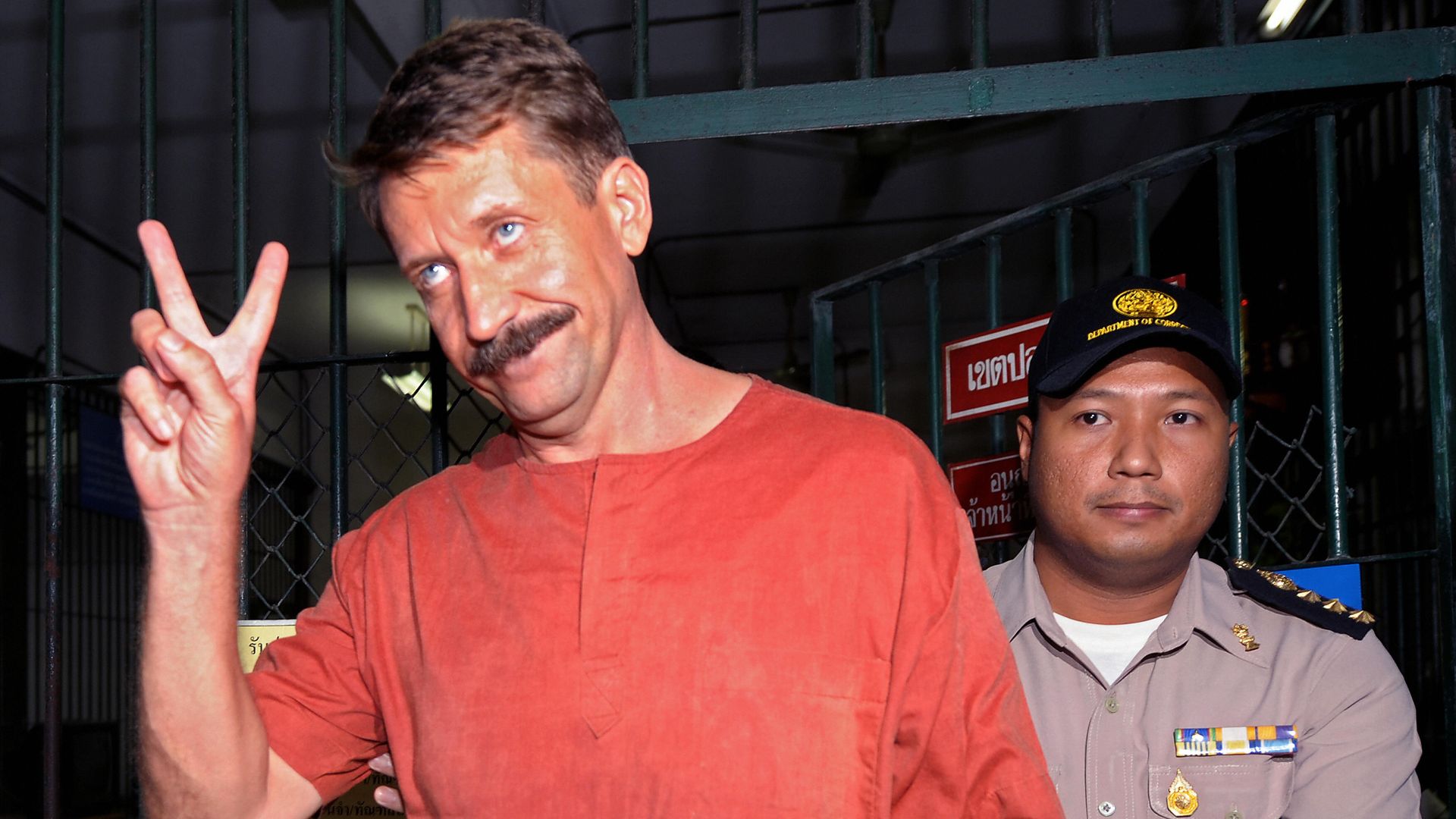 Viktor Bout holds up a peace sign with his right hand as he exits a jail cell.