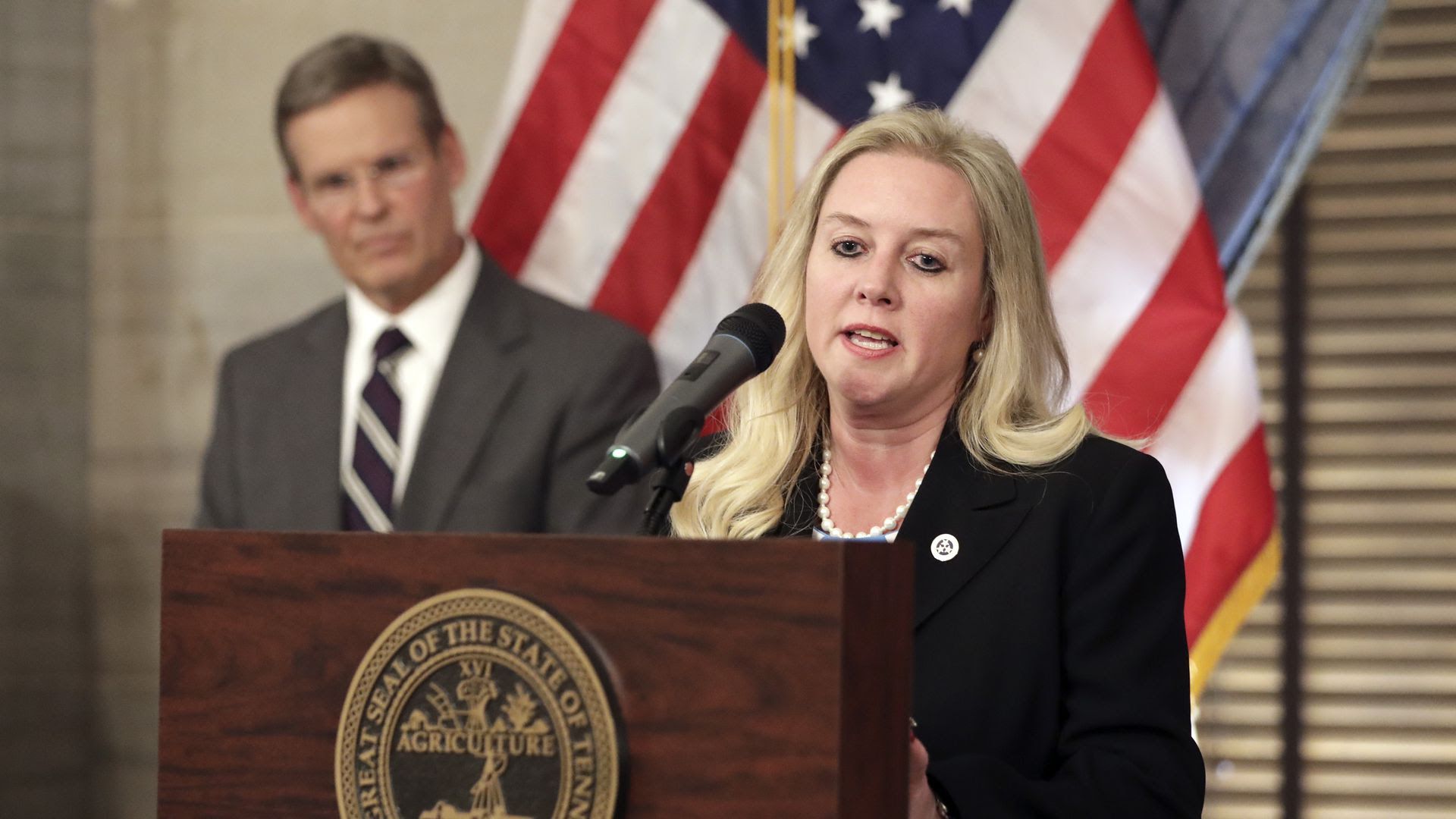 Tennessee health commissioner Lisa Piercey speaking behind a podium in 2020 as Gov. Bill Lee watches.