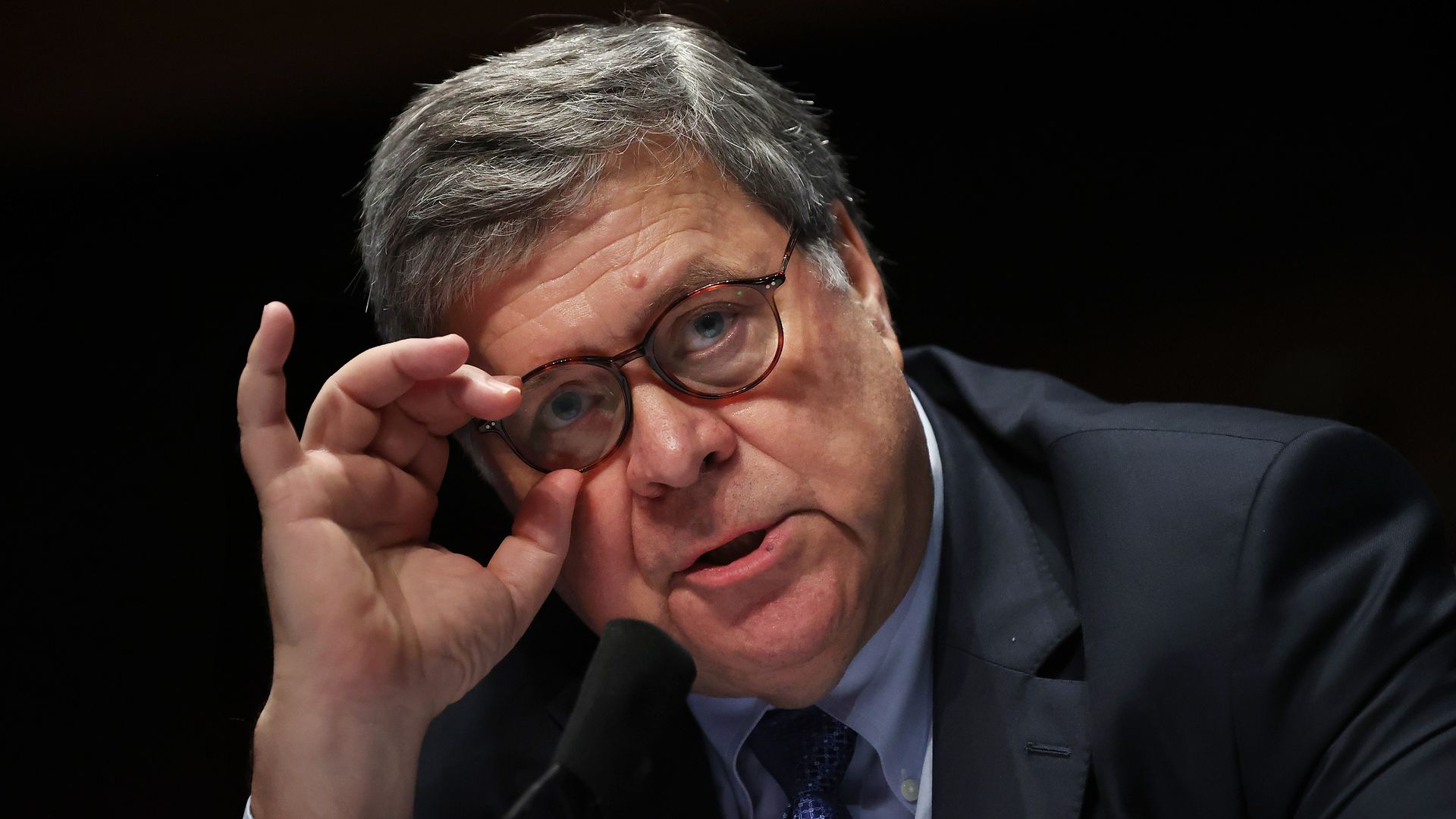 Bill Barr adjusts his glasses while wearing a suit and tie 