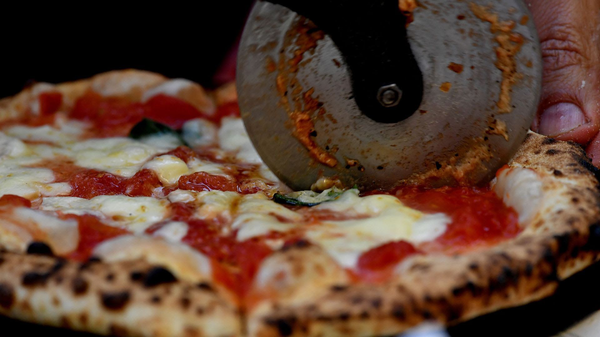 A pizza cutter wheel slices through a pizza.