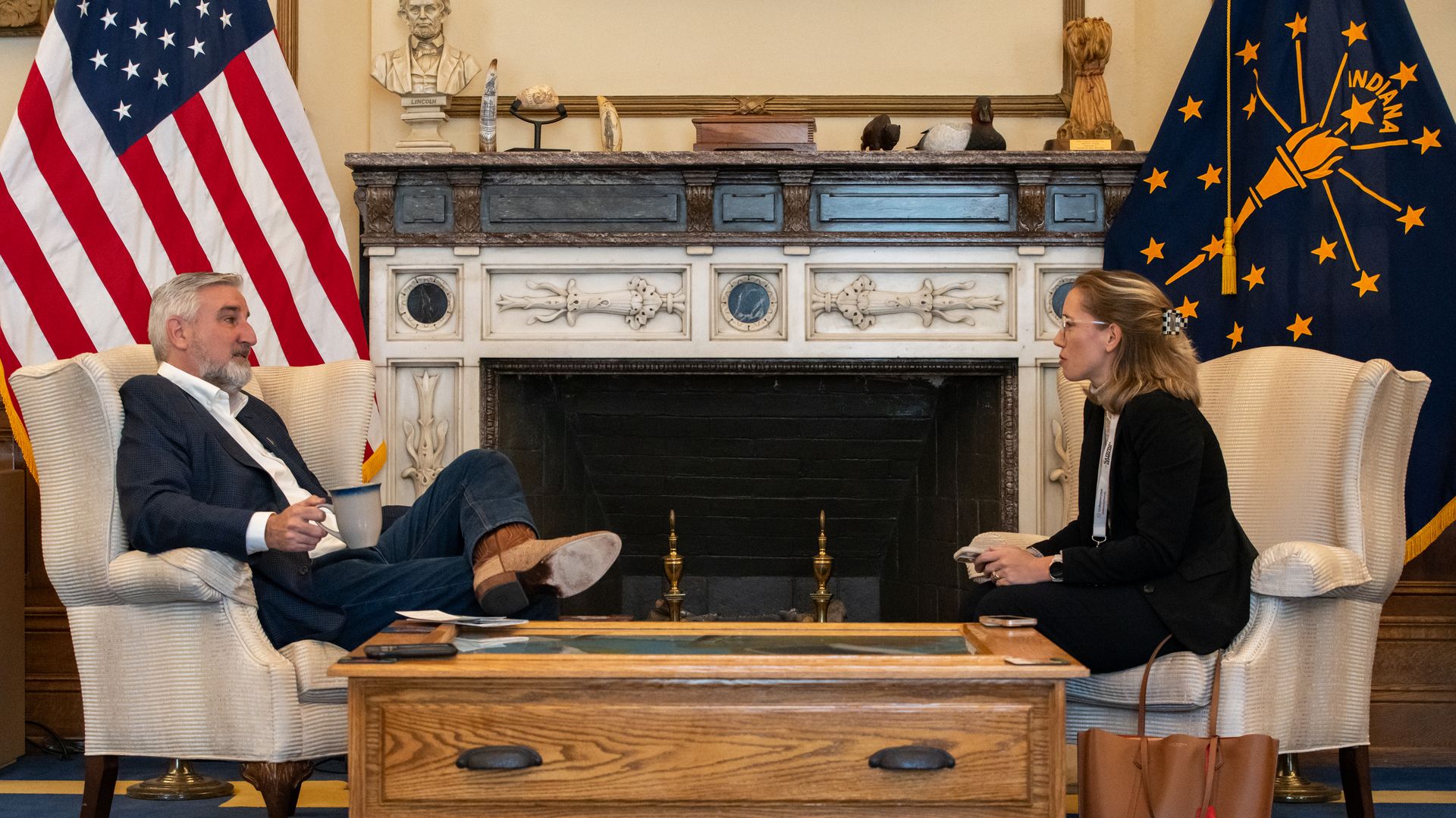 Gov. Eric Holcomb sits across from a reporter in front of a fireplace. 