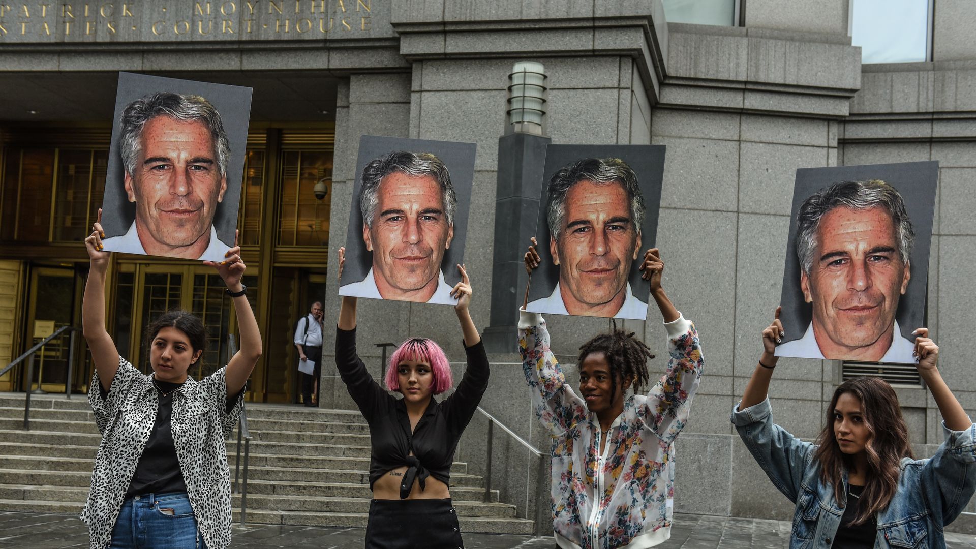 In this image, four people hold up signs of Jeffrey Epstein's face.