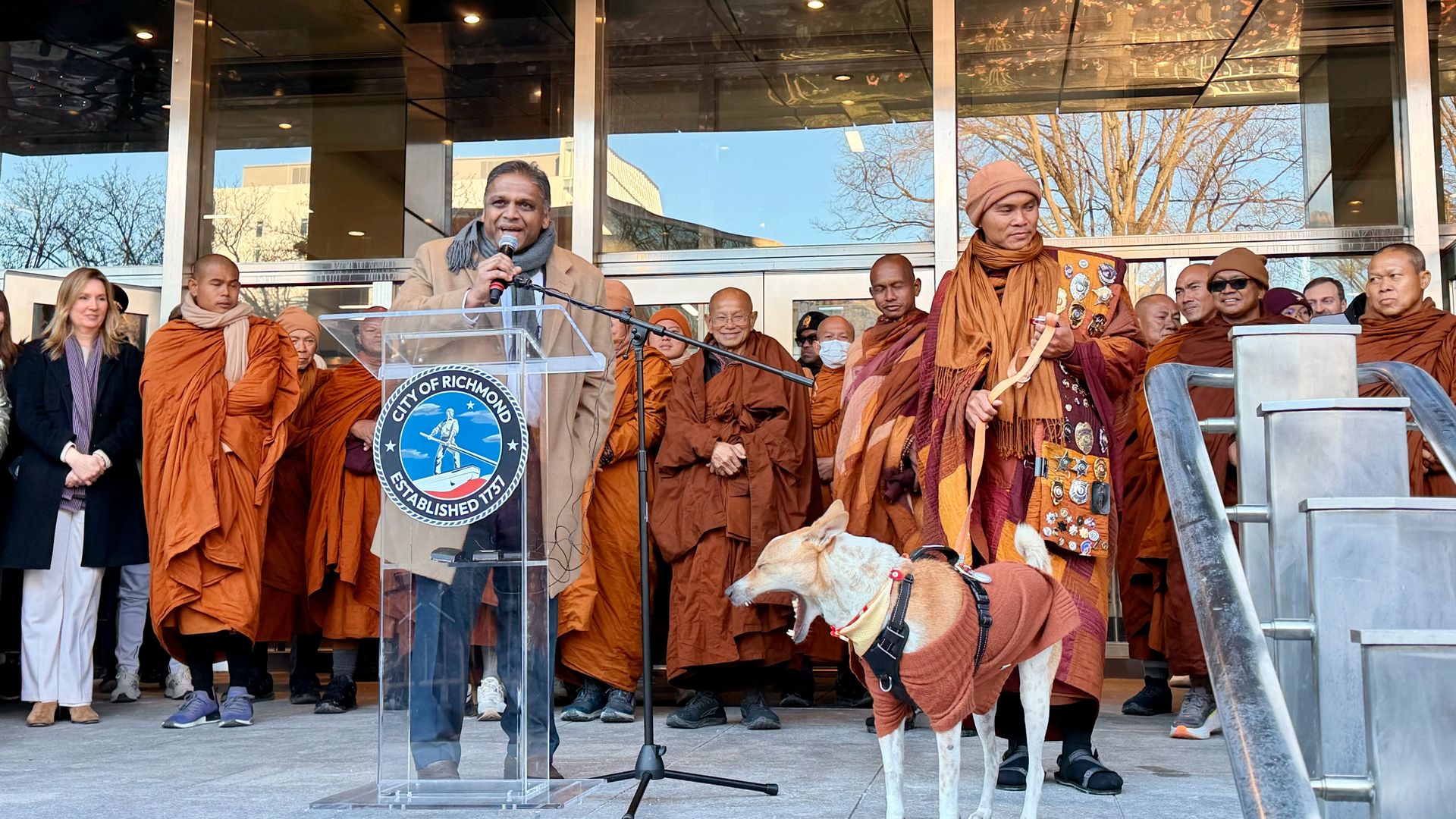 Richmond mayor surrounded by monks where monk clothes and one dog yawning 
