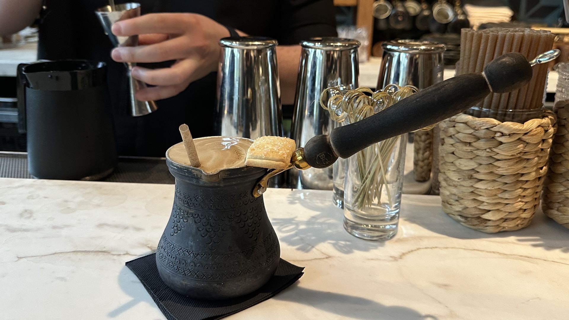 A black briki, or Greek coffee pot, has a boozy drink with Greek coffee and a small shortbread on top at Bar Vlaha.