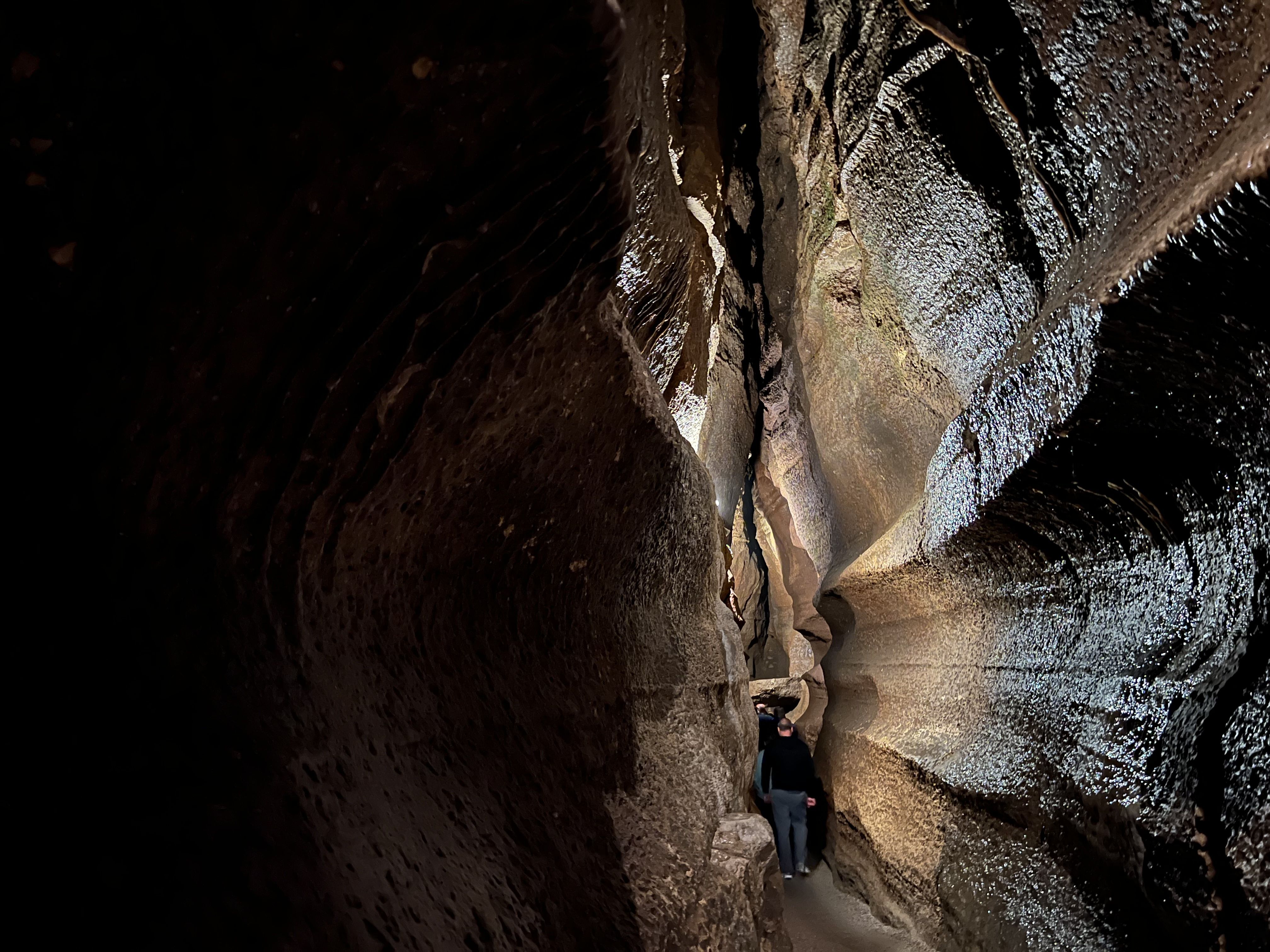 A man walks through a narrow passage of a dimly-lit cave