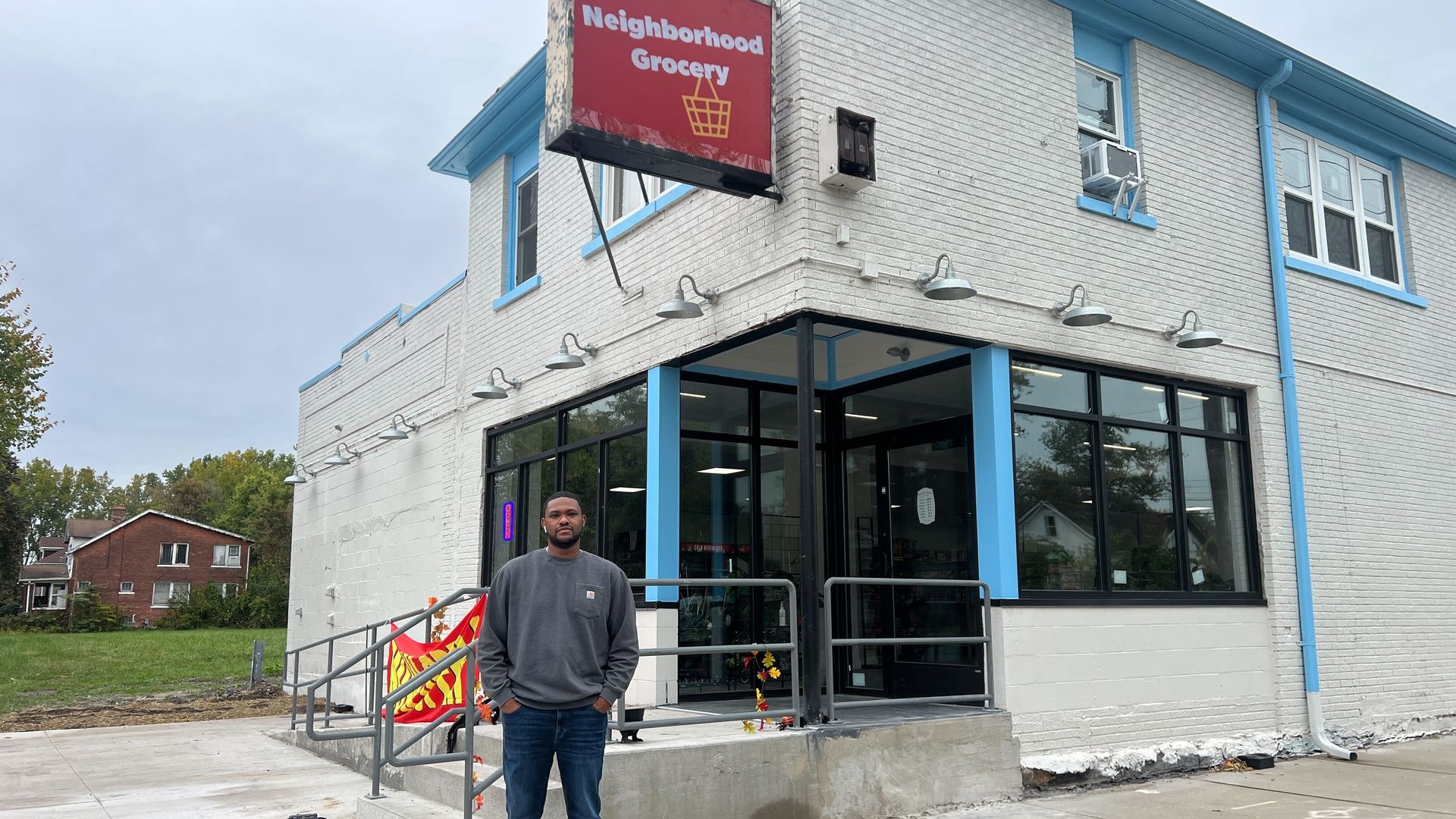 Raphael Wright stands in front of the store. It's in a white, older building with a red sign on top that says "Neighborhood Grocery."