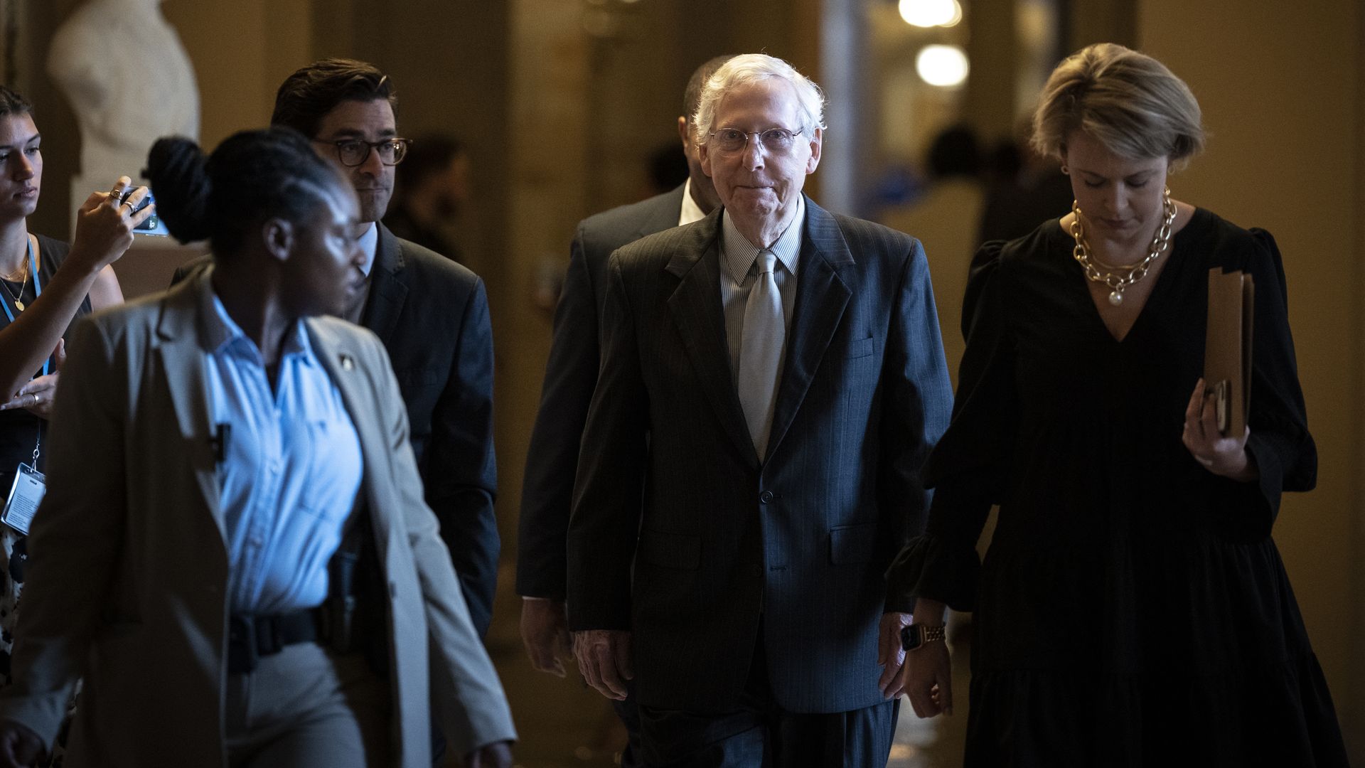 Mitch McConnell walks, leaving his office surrounded by others