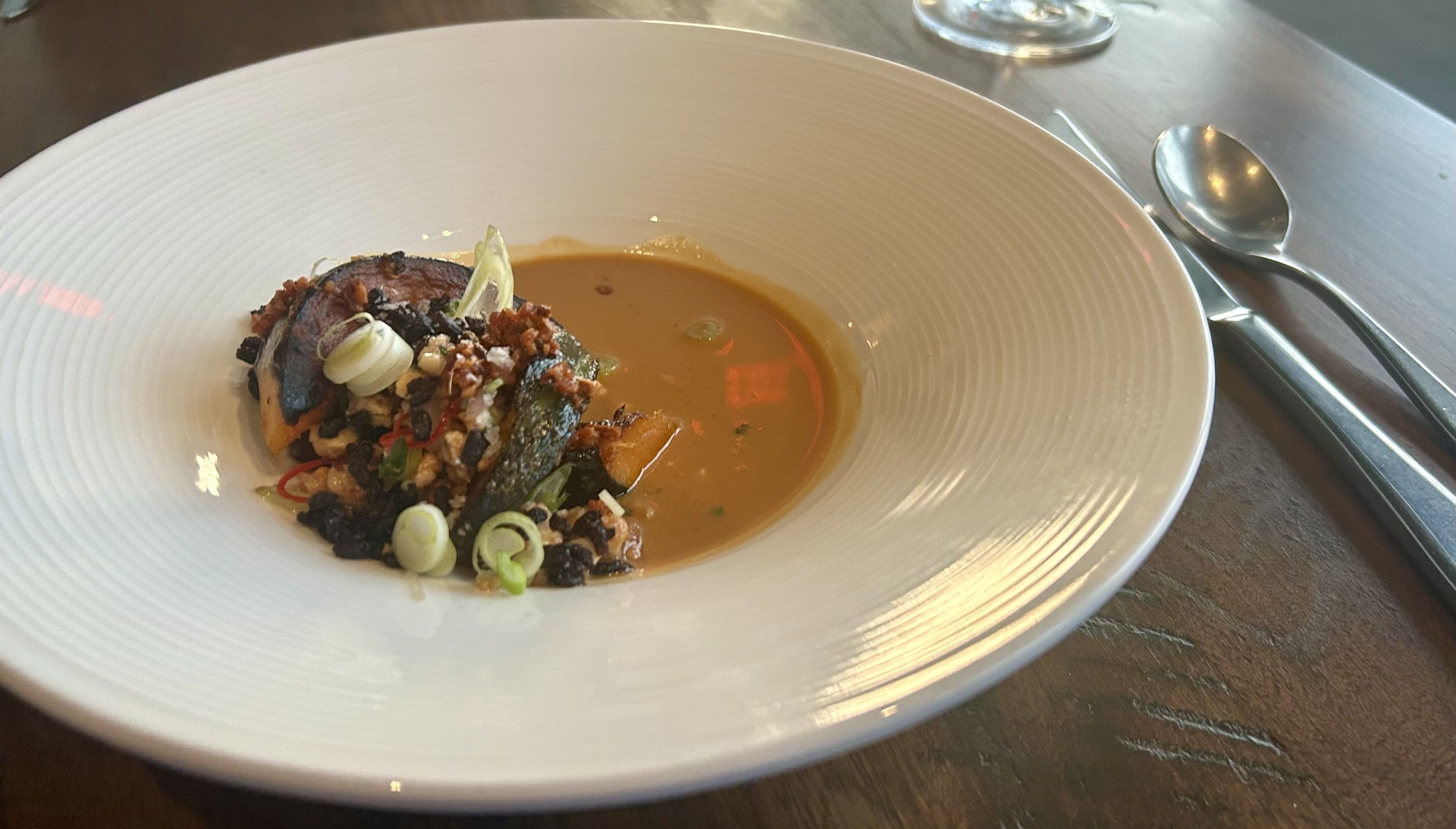 Squash that's charred and covered in herbs sitting in orange curry.