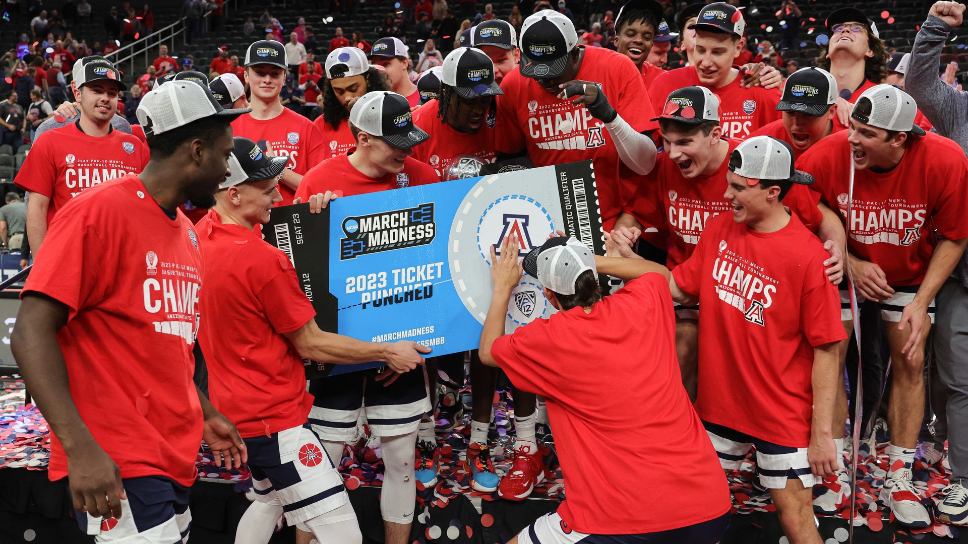 A basketball player signs an oversized ceremonial ticket to the NCAA tournament while his teammates celebrate.