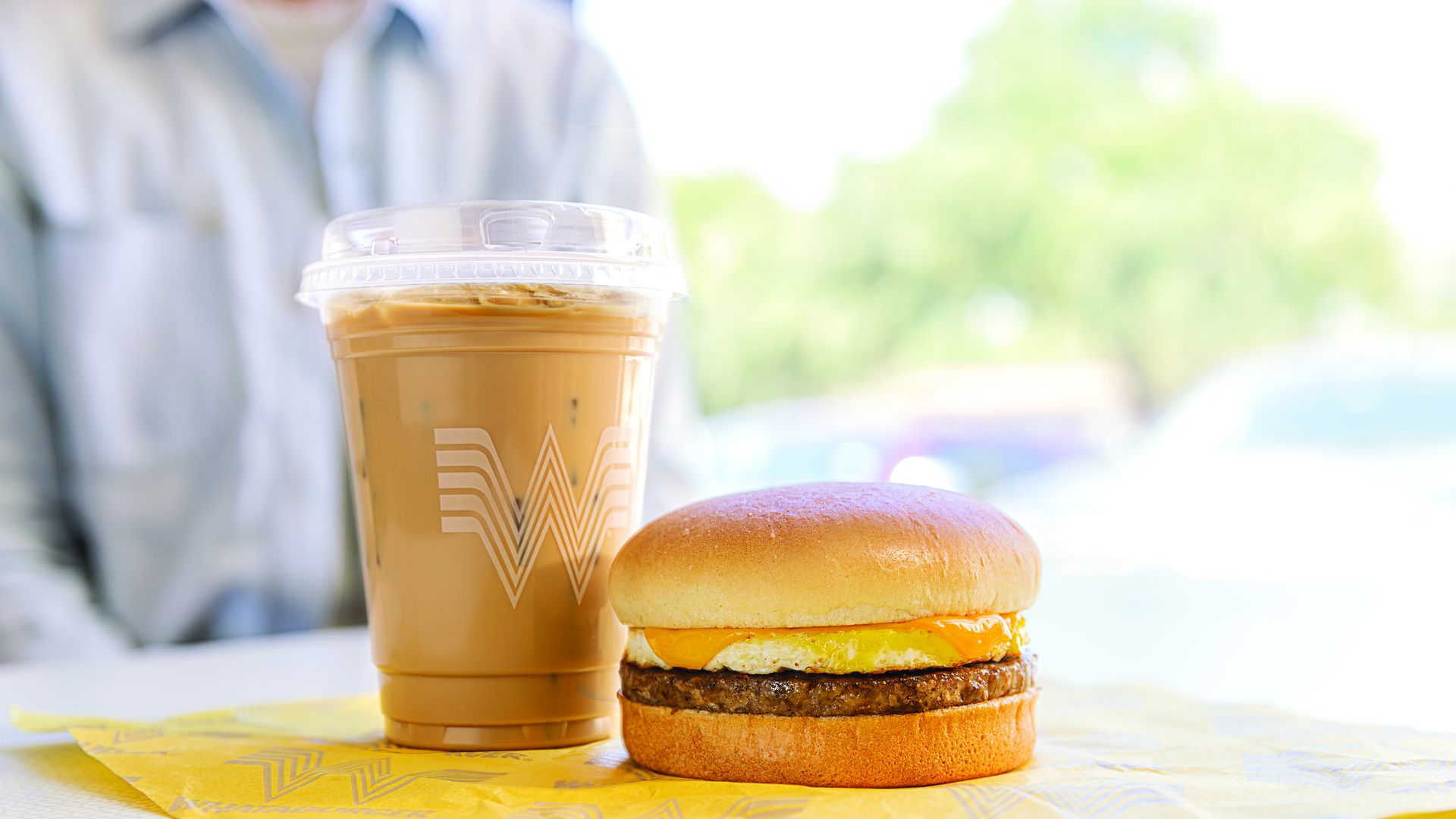 An iced coffee placed next to a breakfast sandwich.