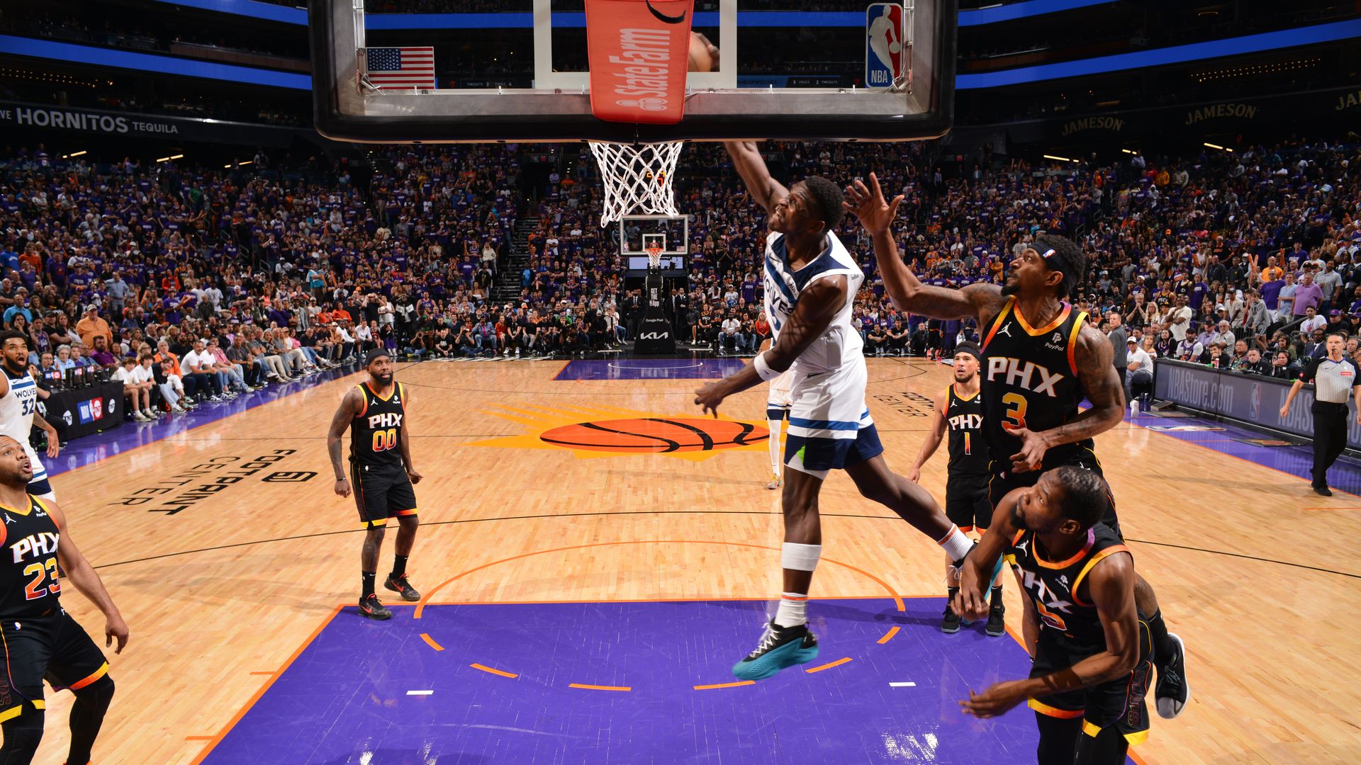 A basketball player in a white jersey goes up for an emphatic dunk with five other players in black jerseys looking on