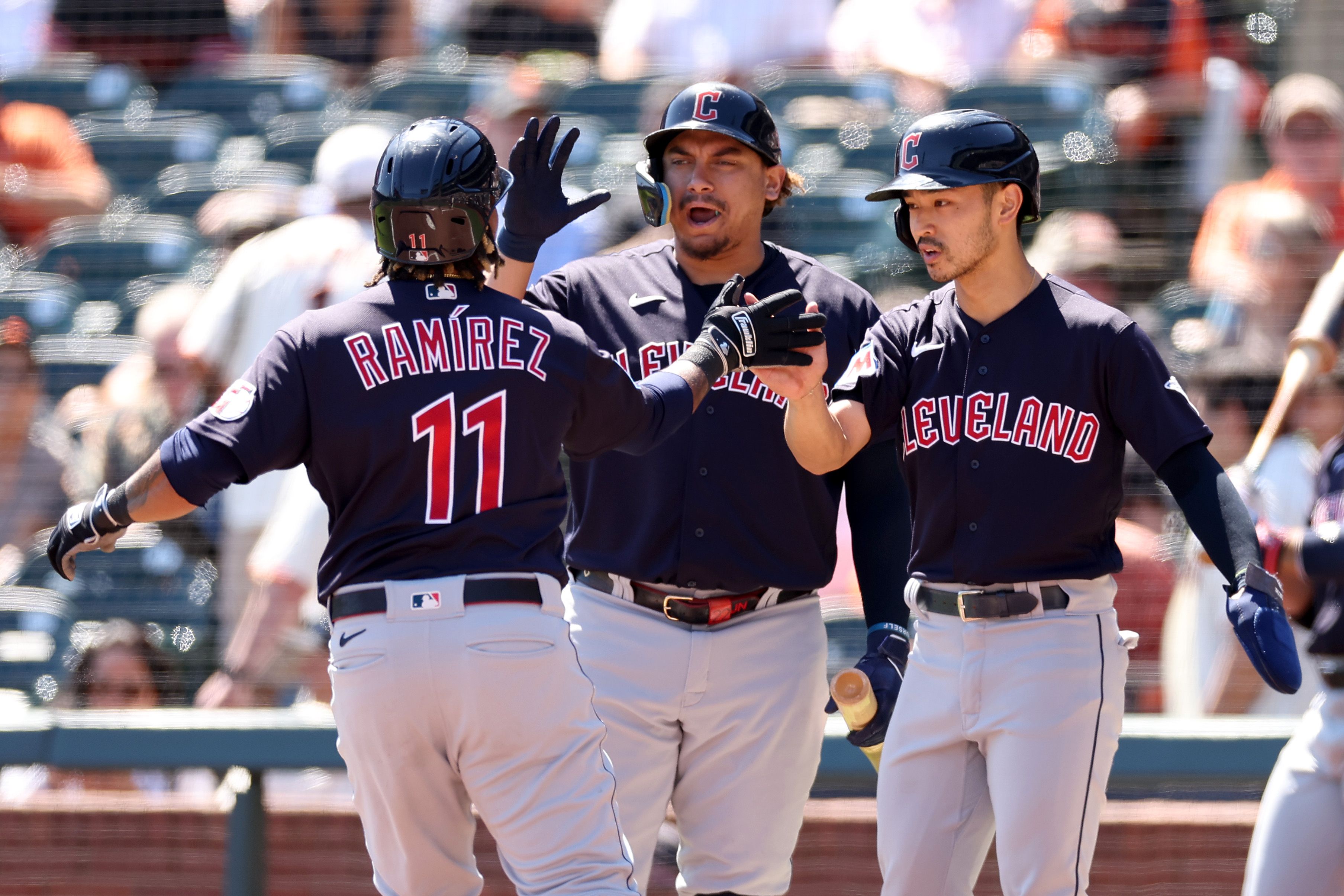 Jose Ramirez, Josh Naylor and Steven Kwan all high-fiving on the baseball field.