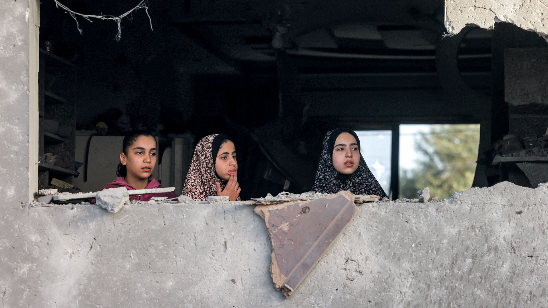 Girls peer through the hole left by a destroyed window from a building in Rafah in the southern Gaza Strip on April 24, 2024 following reported Israeli air strikes overnight amid the ongoing conflict in the Palestinian territory between Israel and the militant group Hamas.