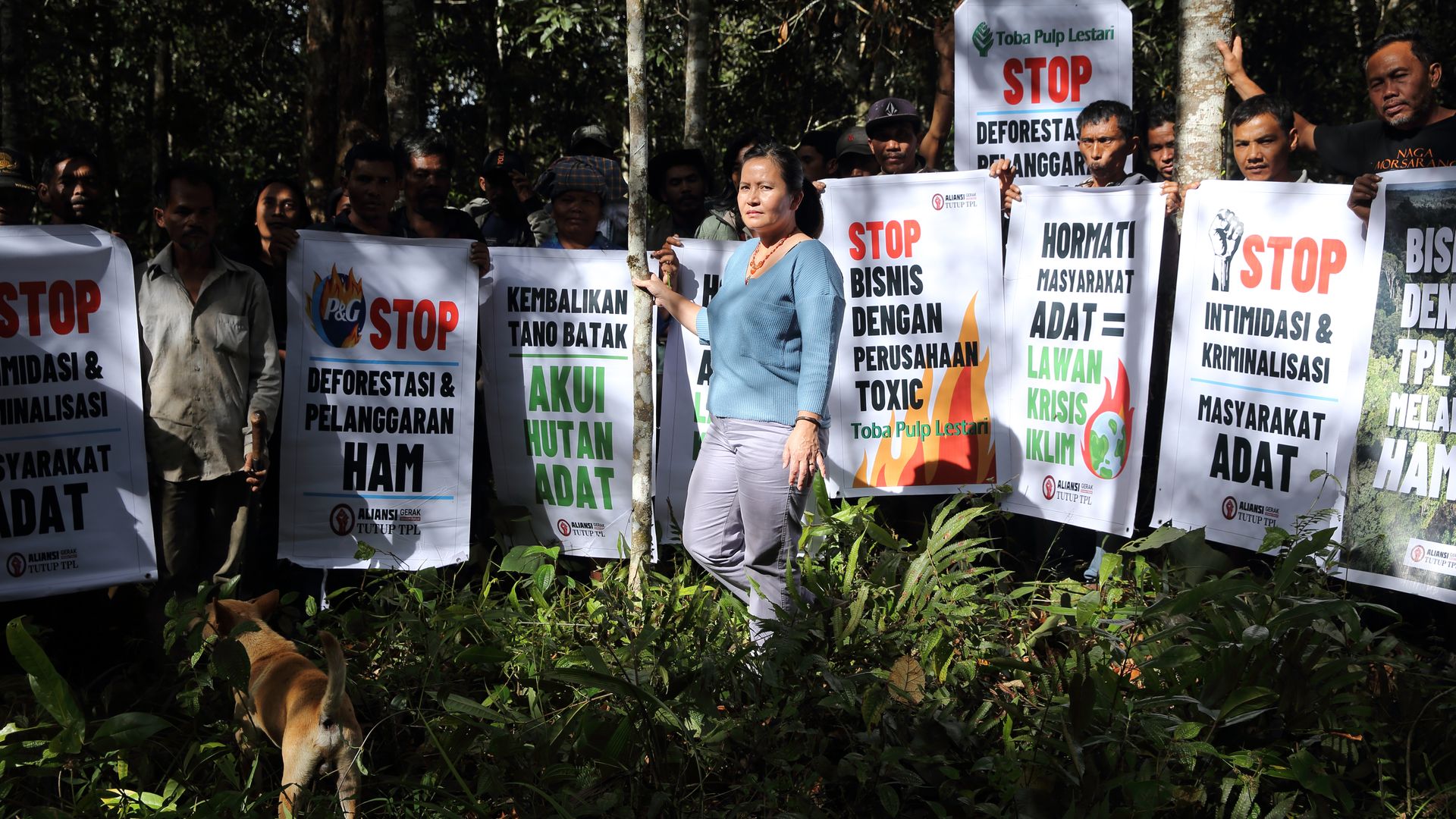 A woman stands in a forest, in a group of people protesting. 
