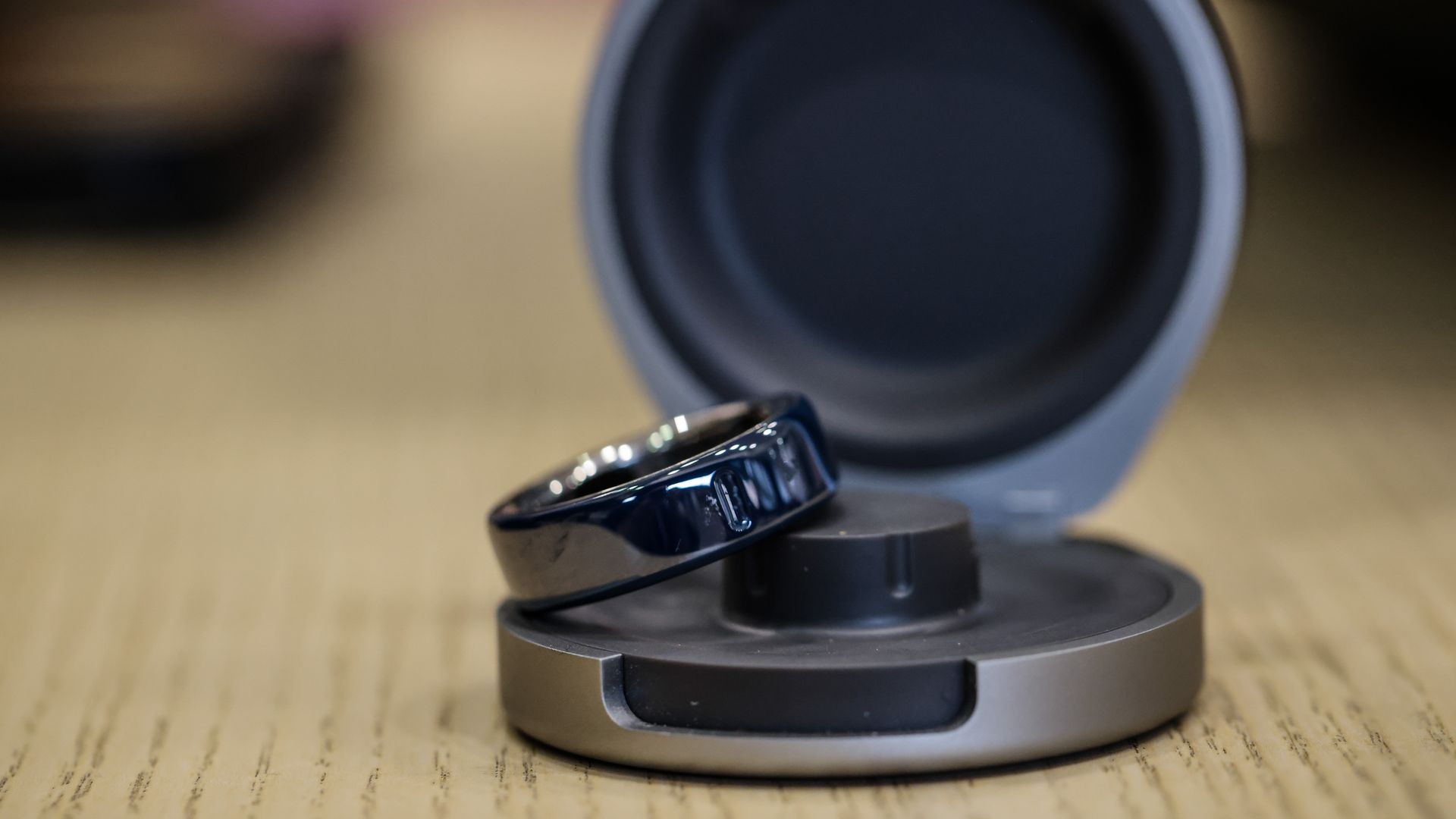 Close-up of a ring on a large, dark circular opening with a light gray rim, mounted on a metallic base on a wooden surface; the background is blurred.
