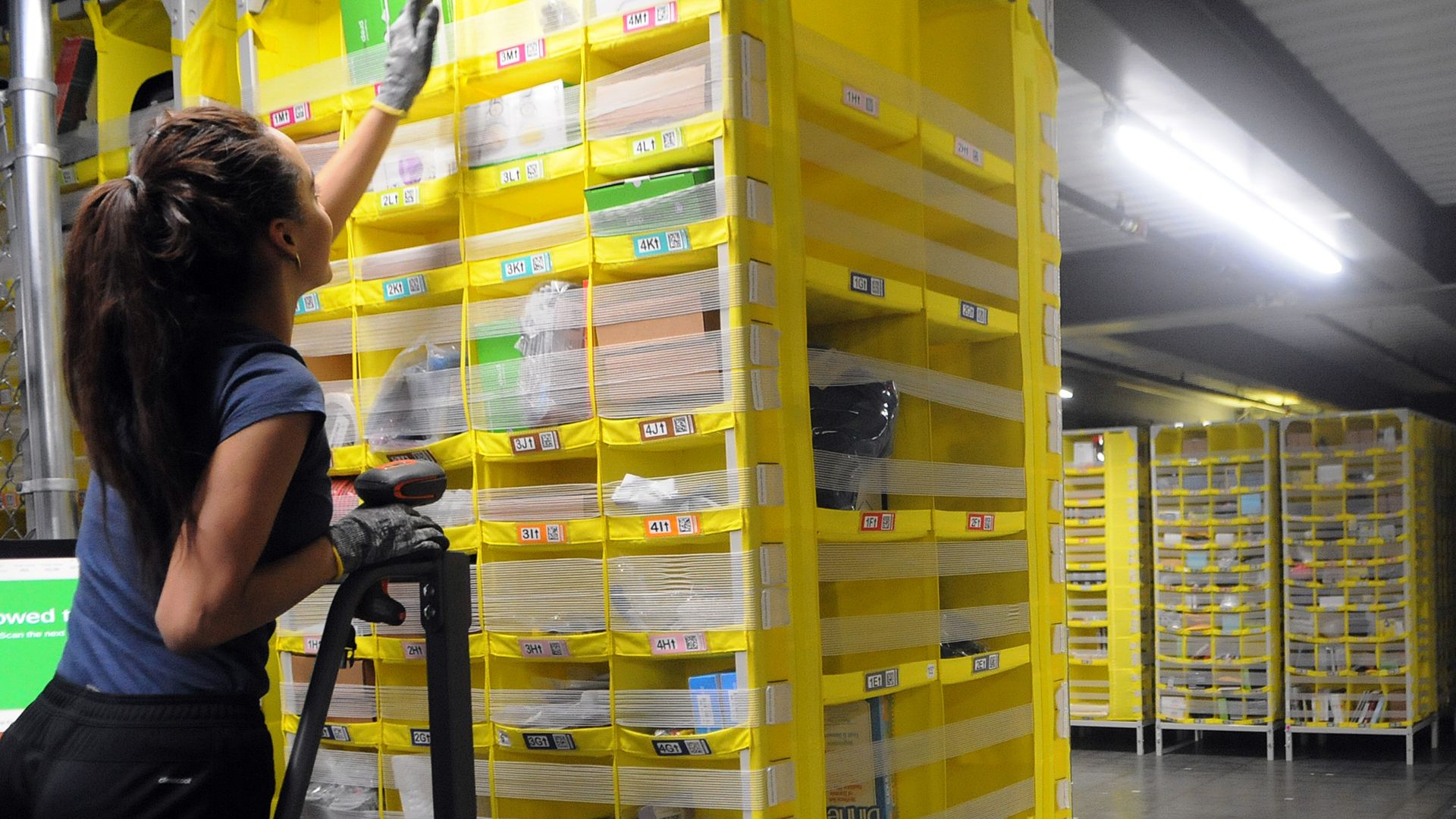 A woman reaches for an item on a shelf in a warehouse