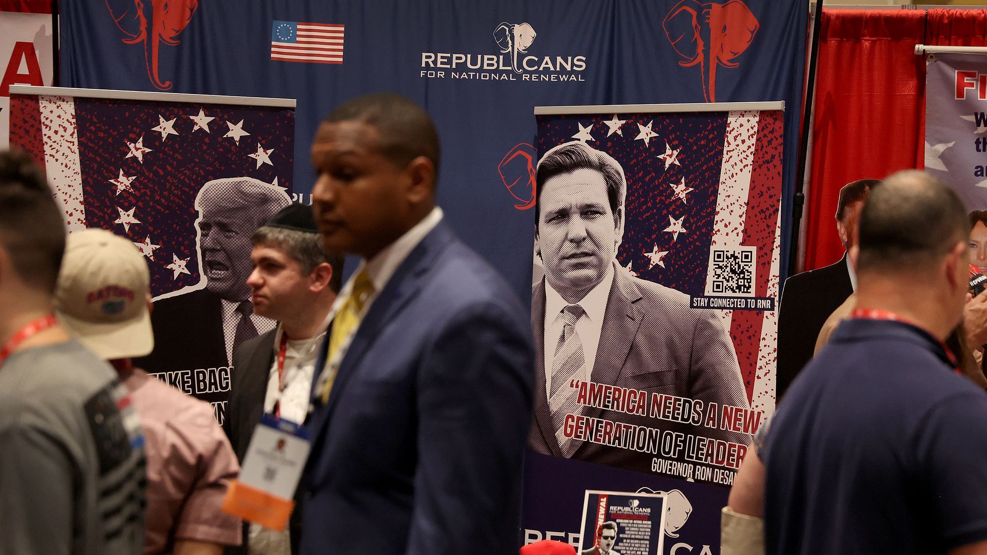 CPAC attendees walk past posters of Donald Trump and Ron DeSantis