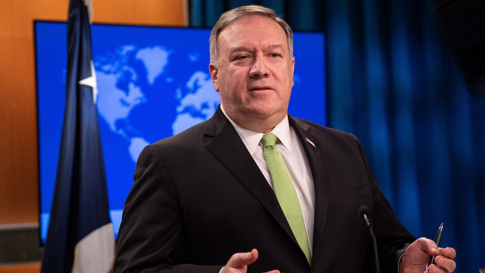 In this image, Pompeo stands in front of a flag and map
