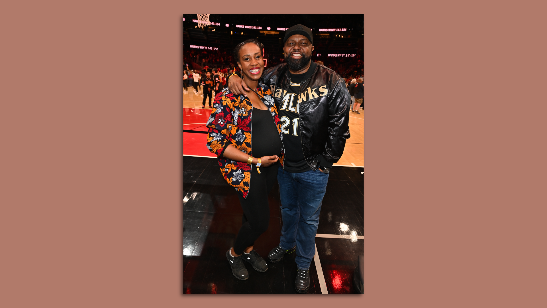 A photo of a couple, one of whom is pregnant, standing and smiling on a basketball court during a game