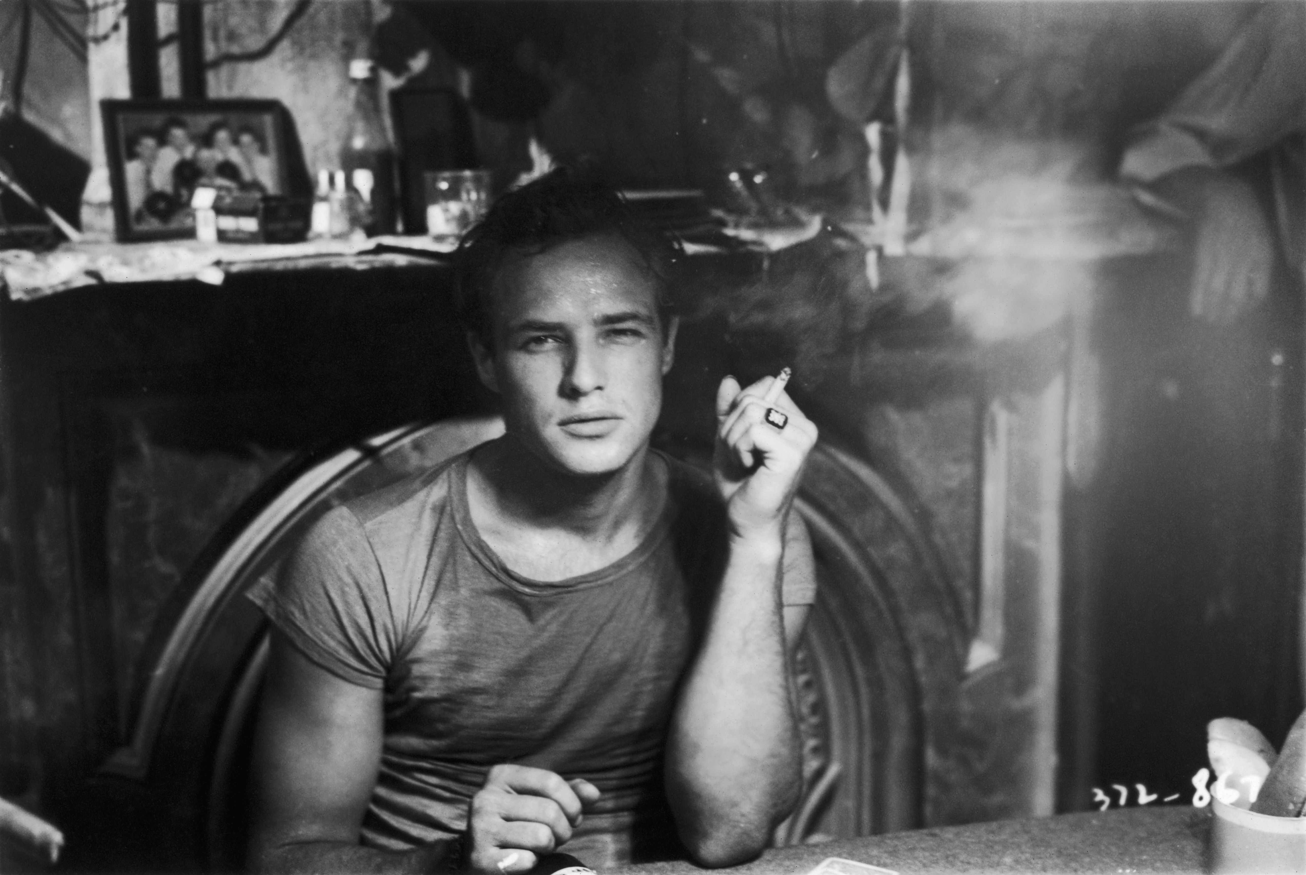 A black and white image of Marlon Brando as he sits in a chair and stares directly at the camera.