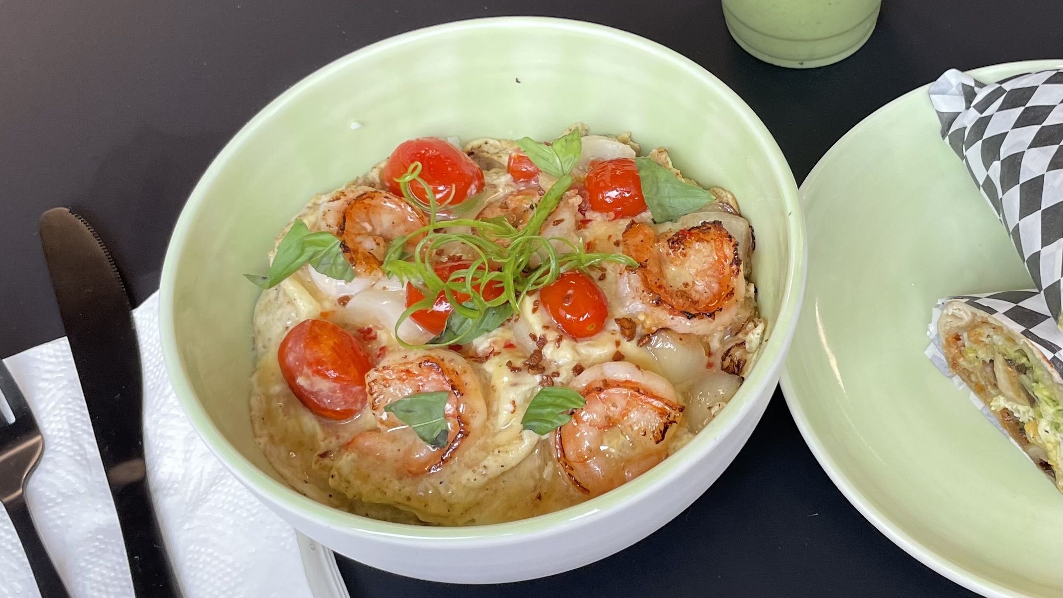 A photo of a green bowl with an omelte on a black tabele.