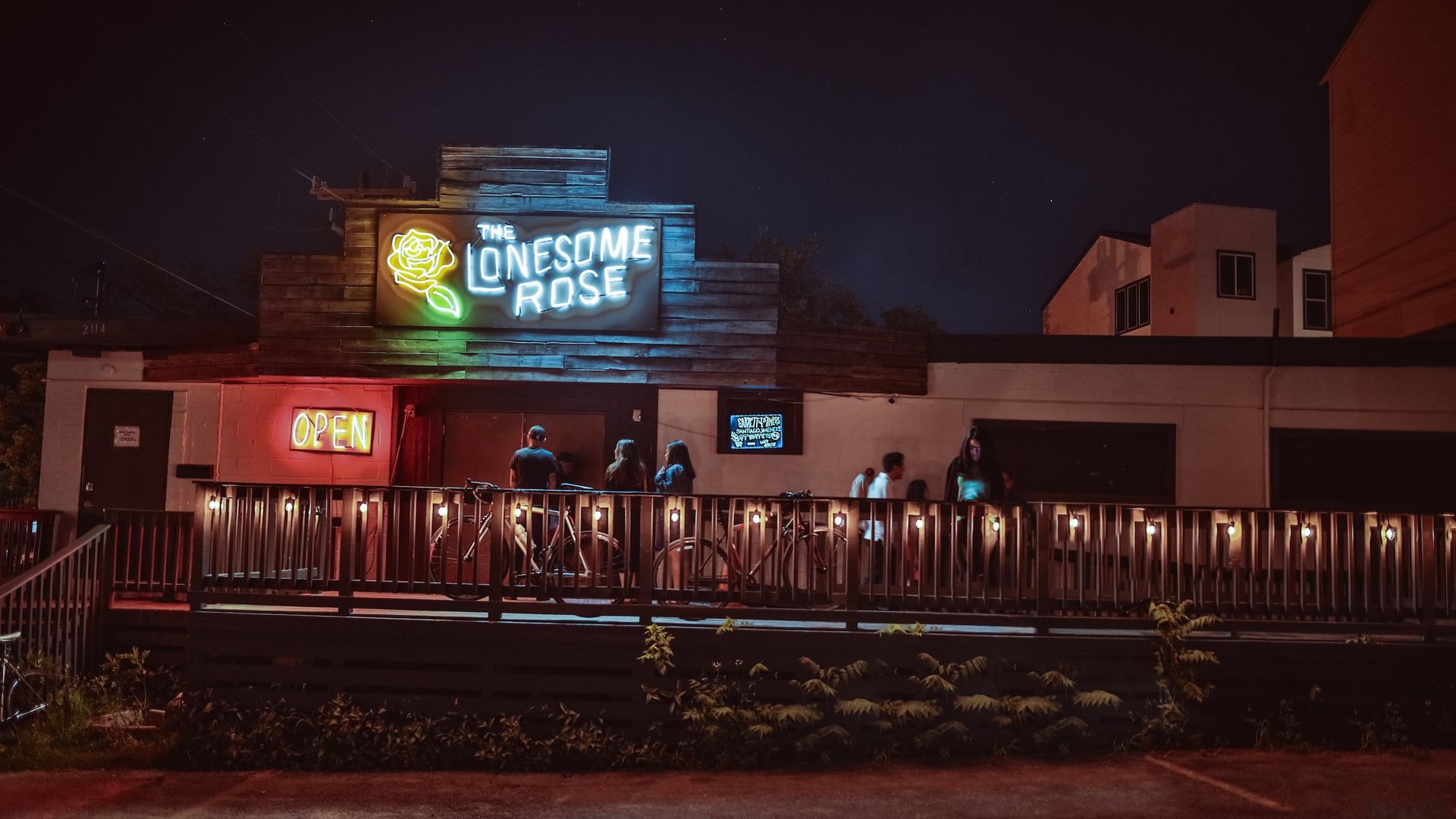 A blue neon sign reads "The Lonesome Rose" next to a neon yellow rose over a bar entrance.