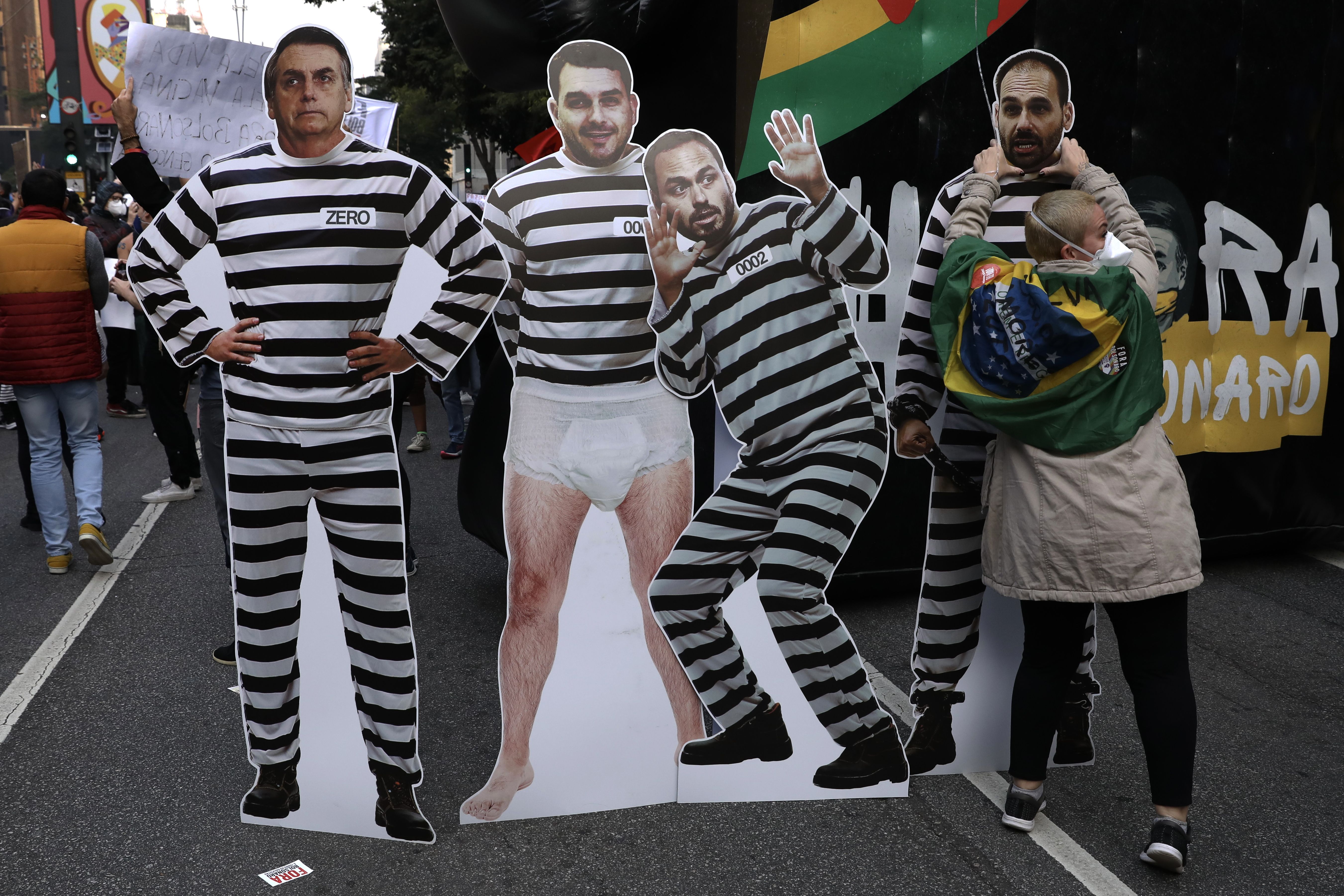 A demonstrator stands with boards depicting Jair Bolsonaro (L) and his son (R) as prisoners during a protest against Bolsonaro's administration on June 19, 2021 in Sao Paulo, Brazil.