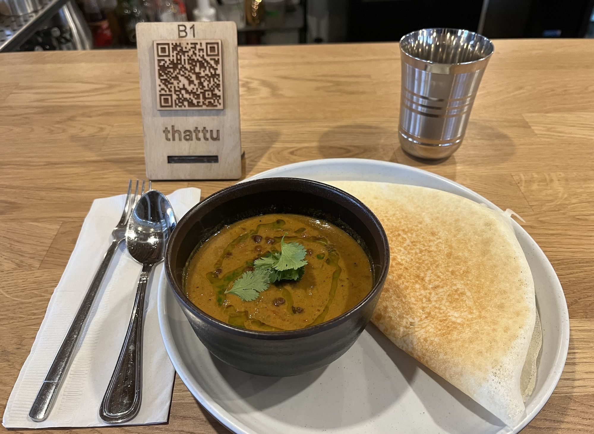 Bowl of curry next to appam on white plate.