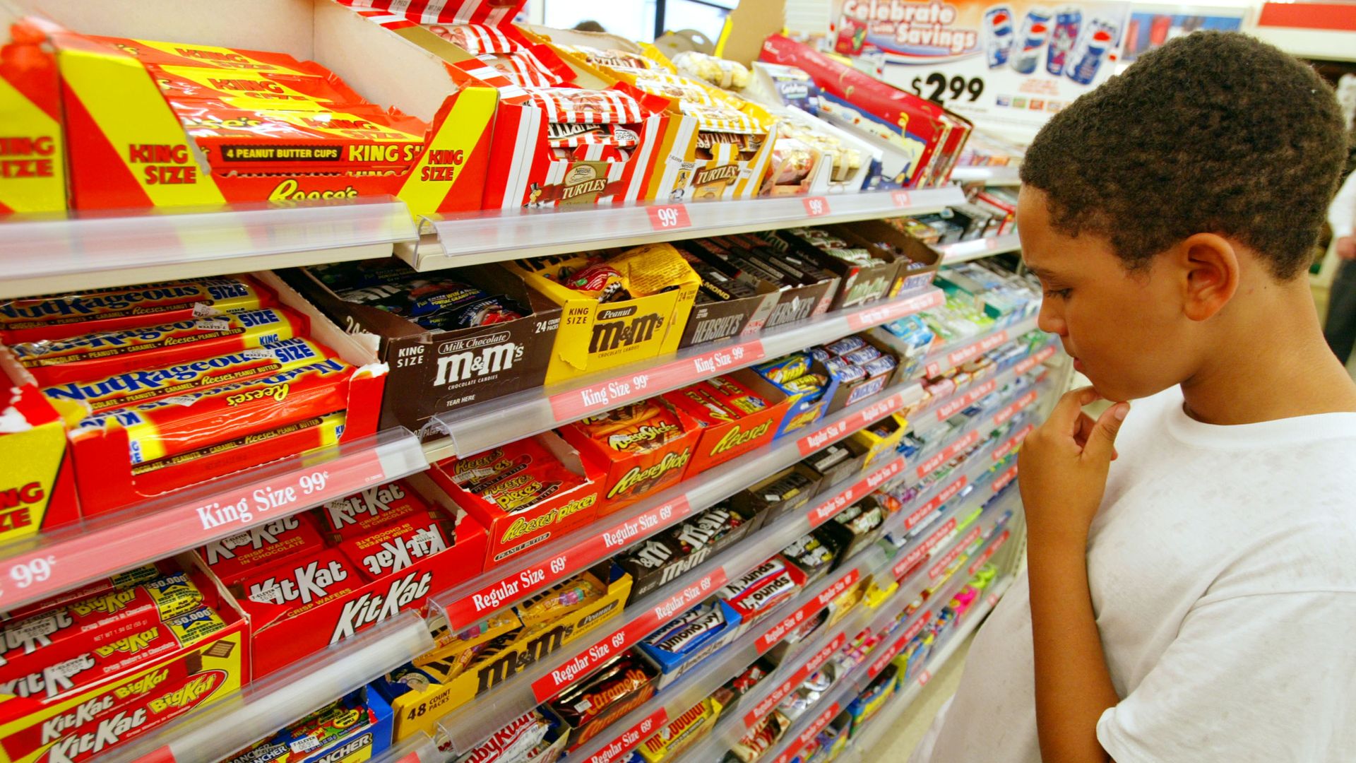 Boy examining a store's rack of chocolate bars and other candy.