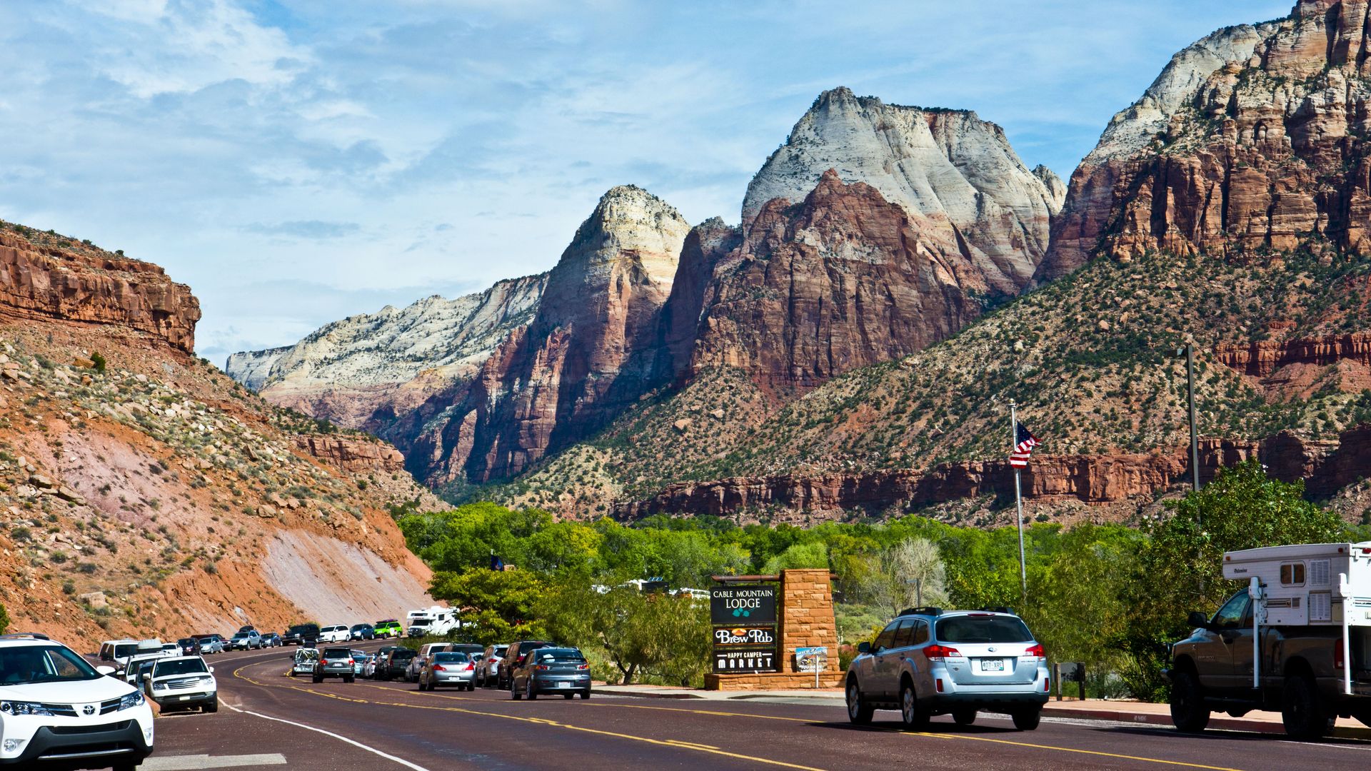 Traffic enters and leaves Zion National Park, with colorful orange and red and tawny mountains in the background