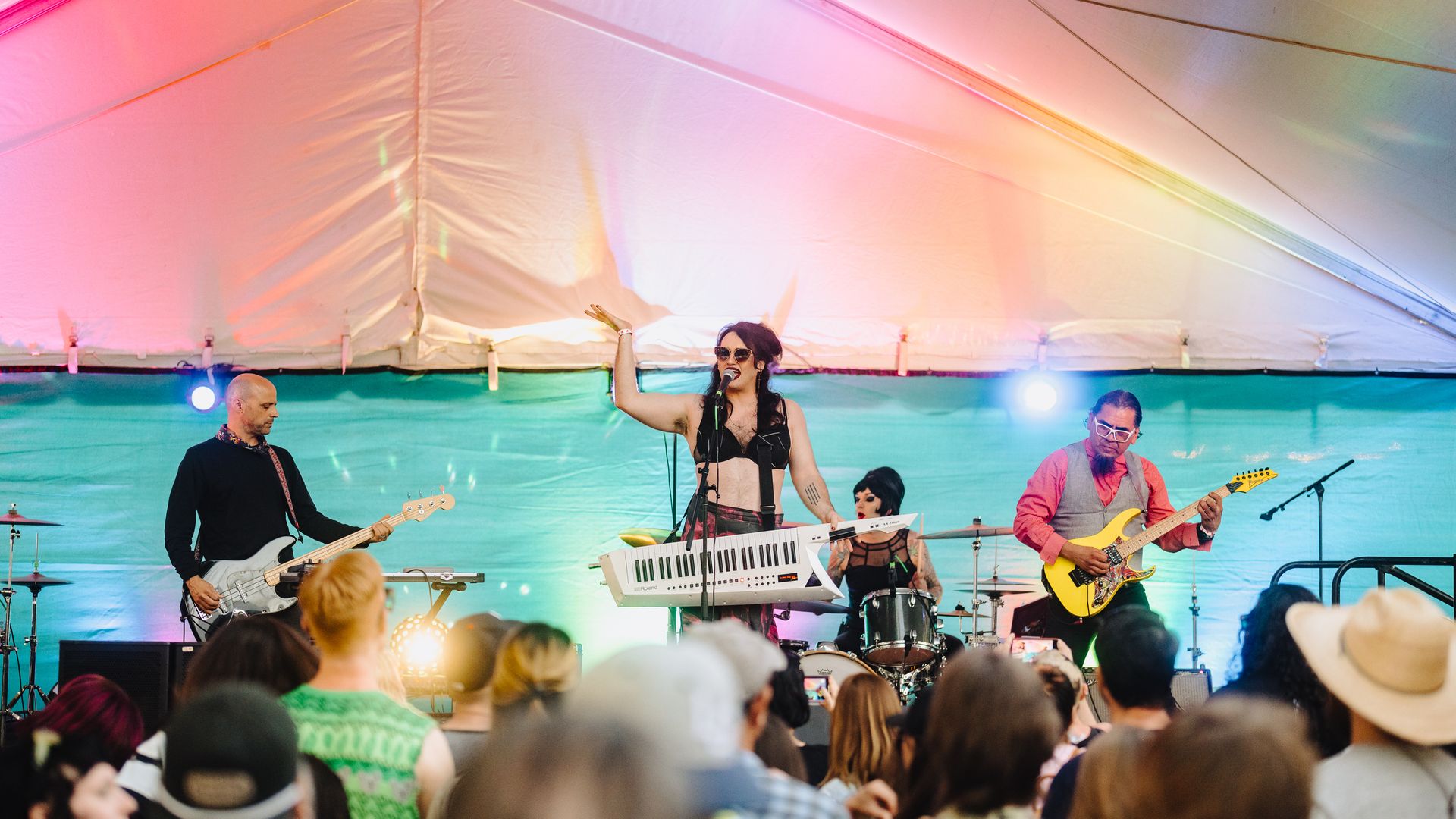 Two guitarists and a singer perform on stage while a crowd watches in the foreground.