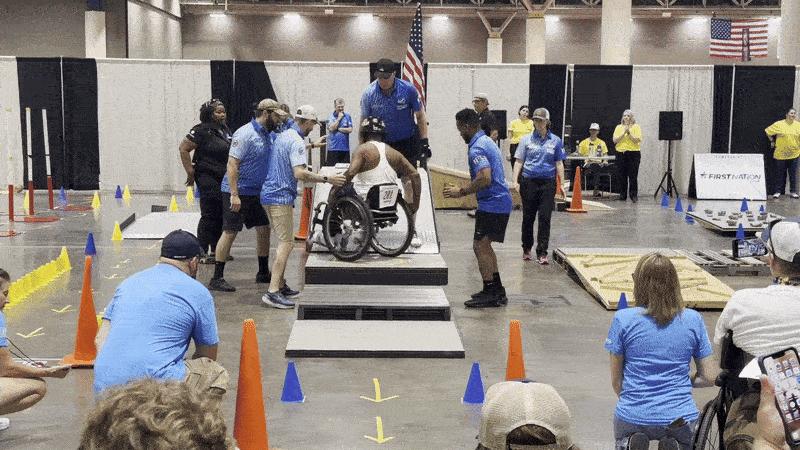 A wheelchair user rolls down a ramp and crosses a finish line, showing relief.